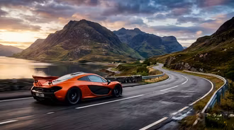 McLaren P1 Sunset Coastal Mountain Drive - A striking cinematic photography shot of a metallic volcano orange McLaren P1 hypercar cruising along a winding coastal road at sunset, framed by rugged green mountain peaks, calm lake water, and dramatic cloud formations.