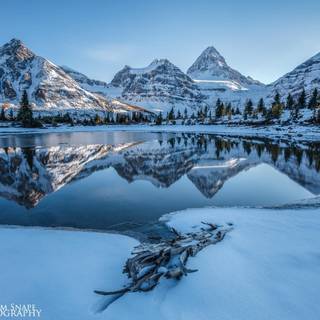 Munți înzăpeziți sărutați de ger care se reflectă pe un lac înghețat