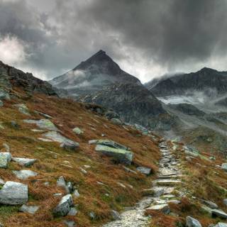 Câmp cu iarbă verde lângă munte sub cer înnorat în timpul zilei 