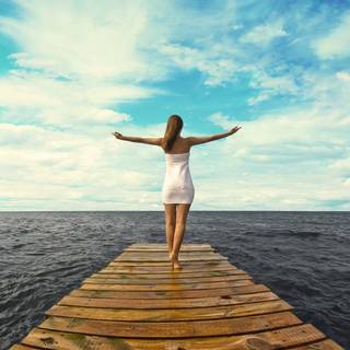 o femeie stând pe un ponton de lemn privind spre orizontul mării