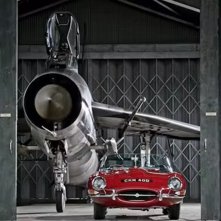 Jaguar E-Type roșu clasic parcat în fața unui avion de vânătoare English 