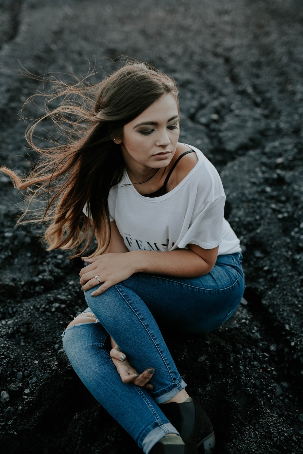 Woman Wearing Scoop Neck Shirt And Distressed Jeans Sitting On Ground While Holding Knee Photo