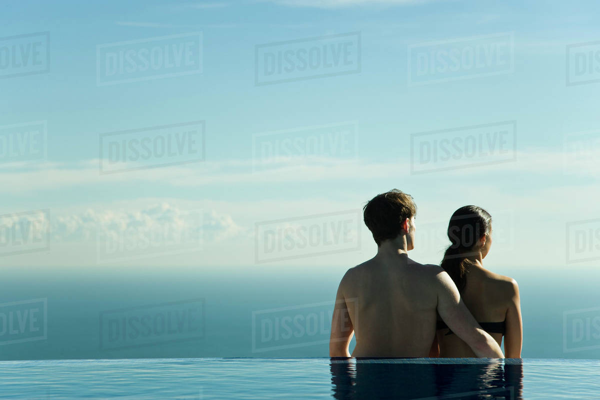 Couple standing at edge of infinity pool, looking at view