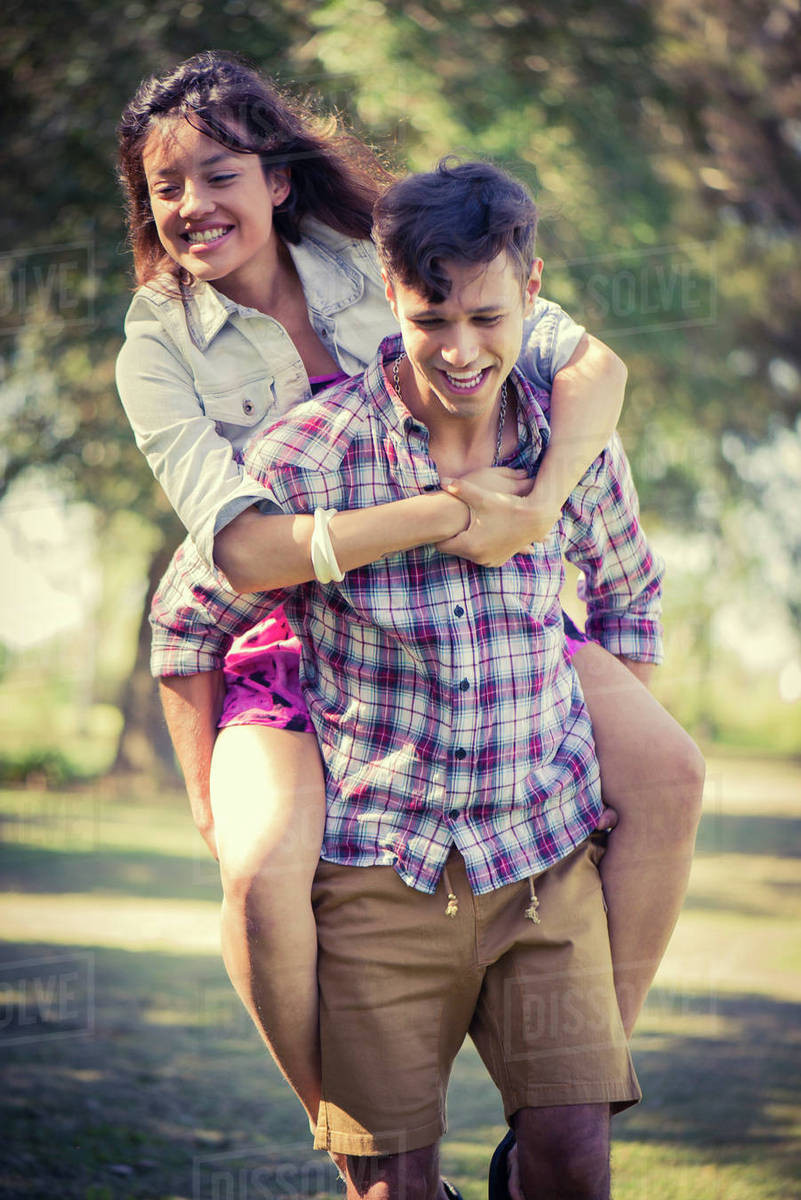 Man giving girlfriend piggyback ride in park