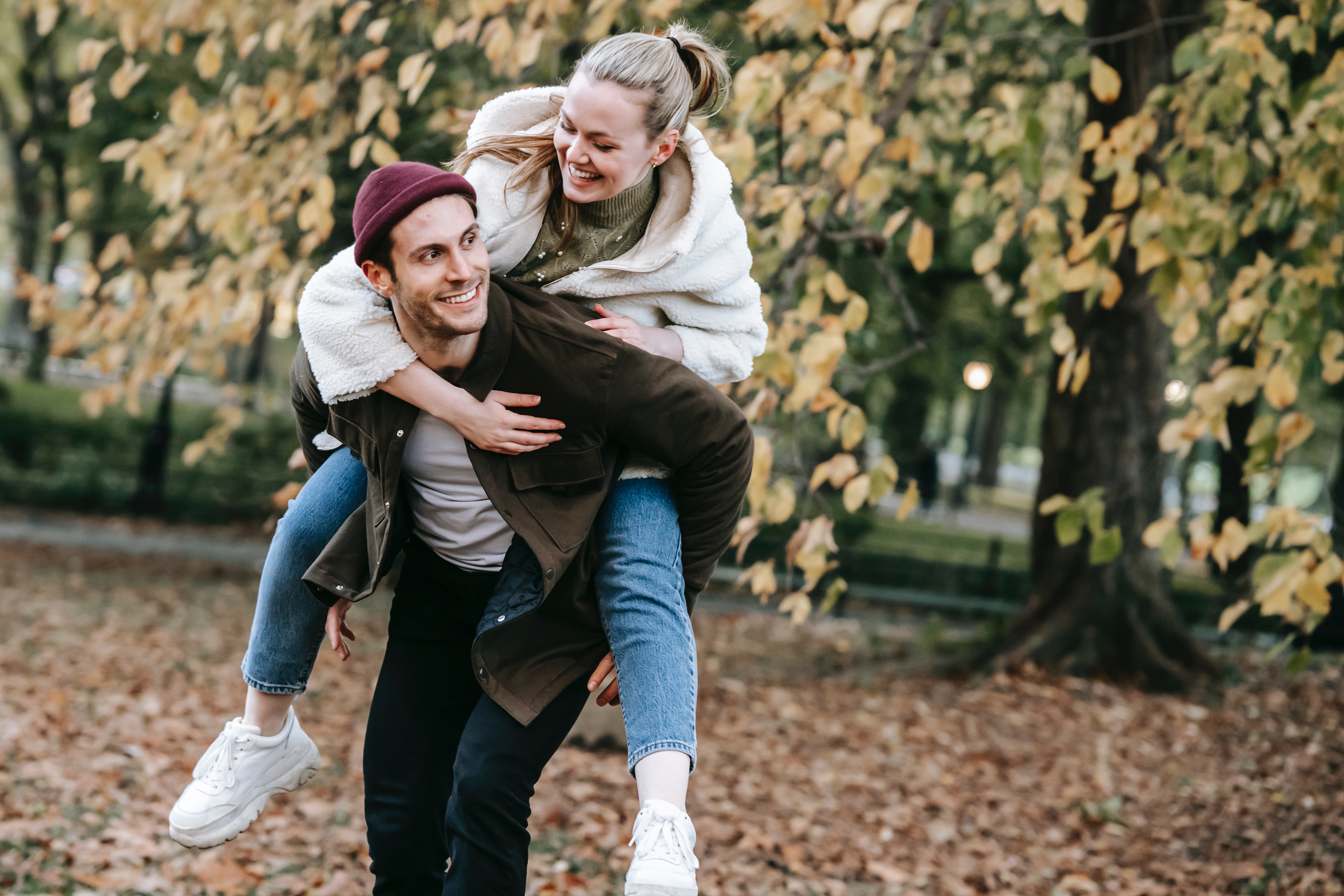 Cheerful man giving piggyback ride to smiling girlfriend in park in autumn · Free