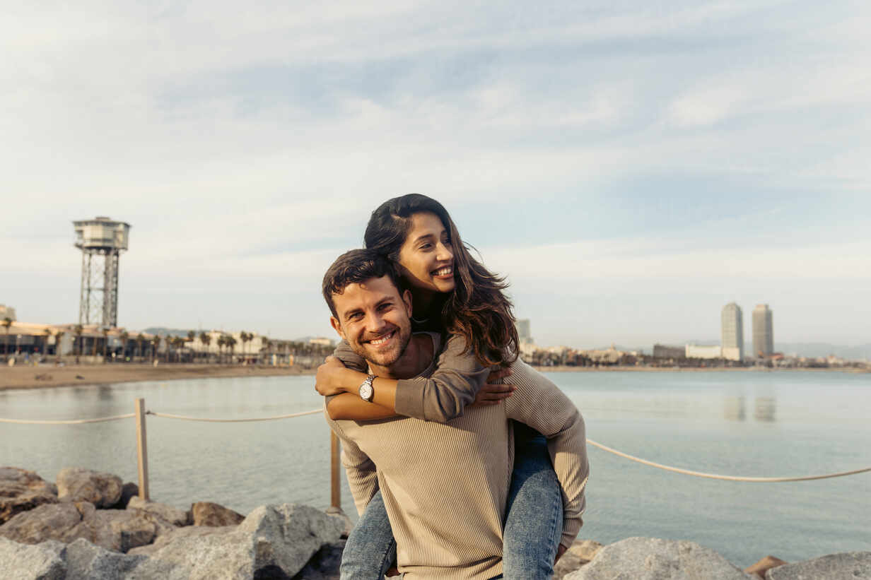 Smiling boyfriend giving piggyback ride to girlfriend against sea and sky