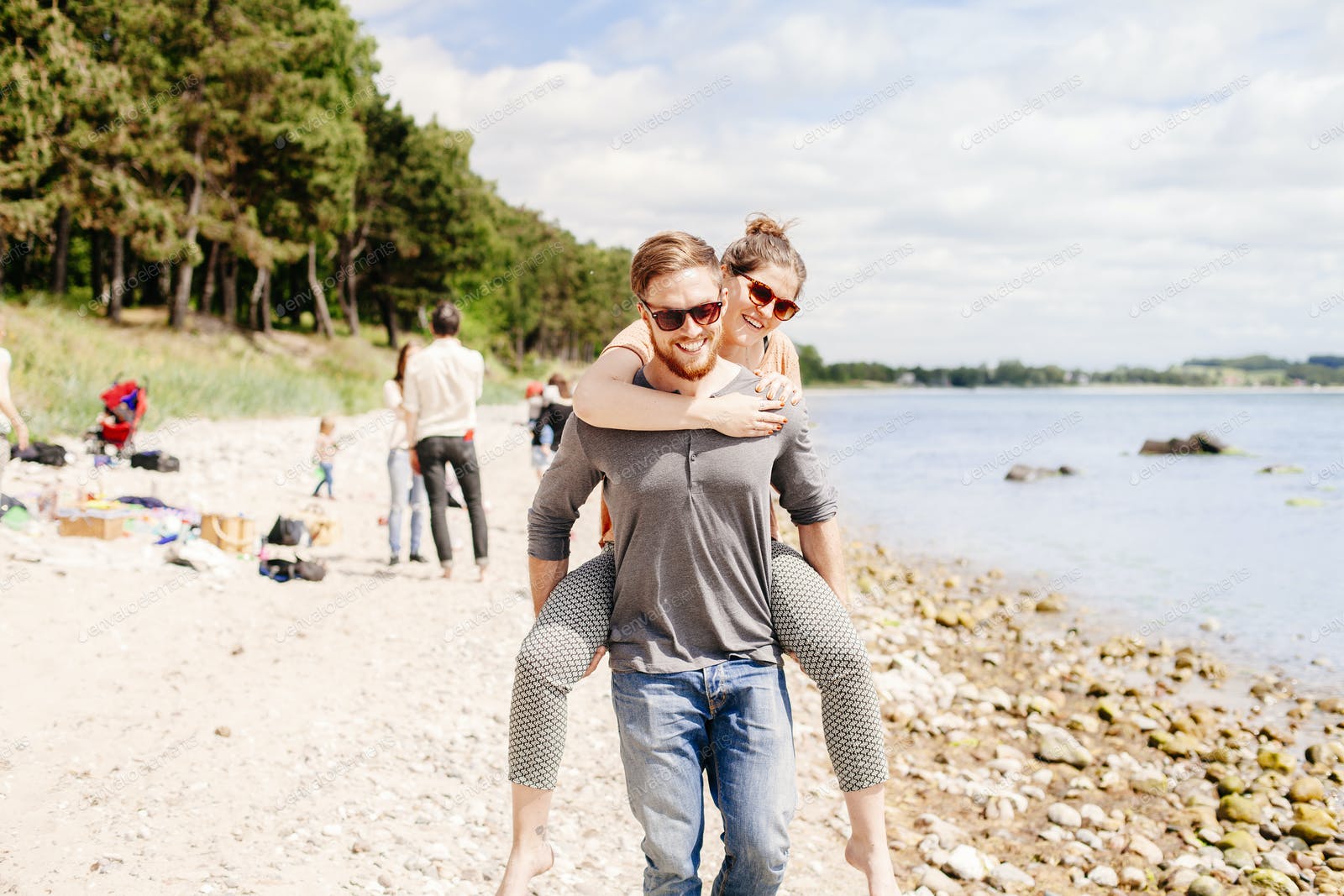 Man giving girlfriend piggyback ride on beach photo by astrakanimage on Envato Elements