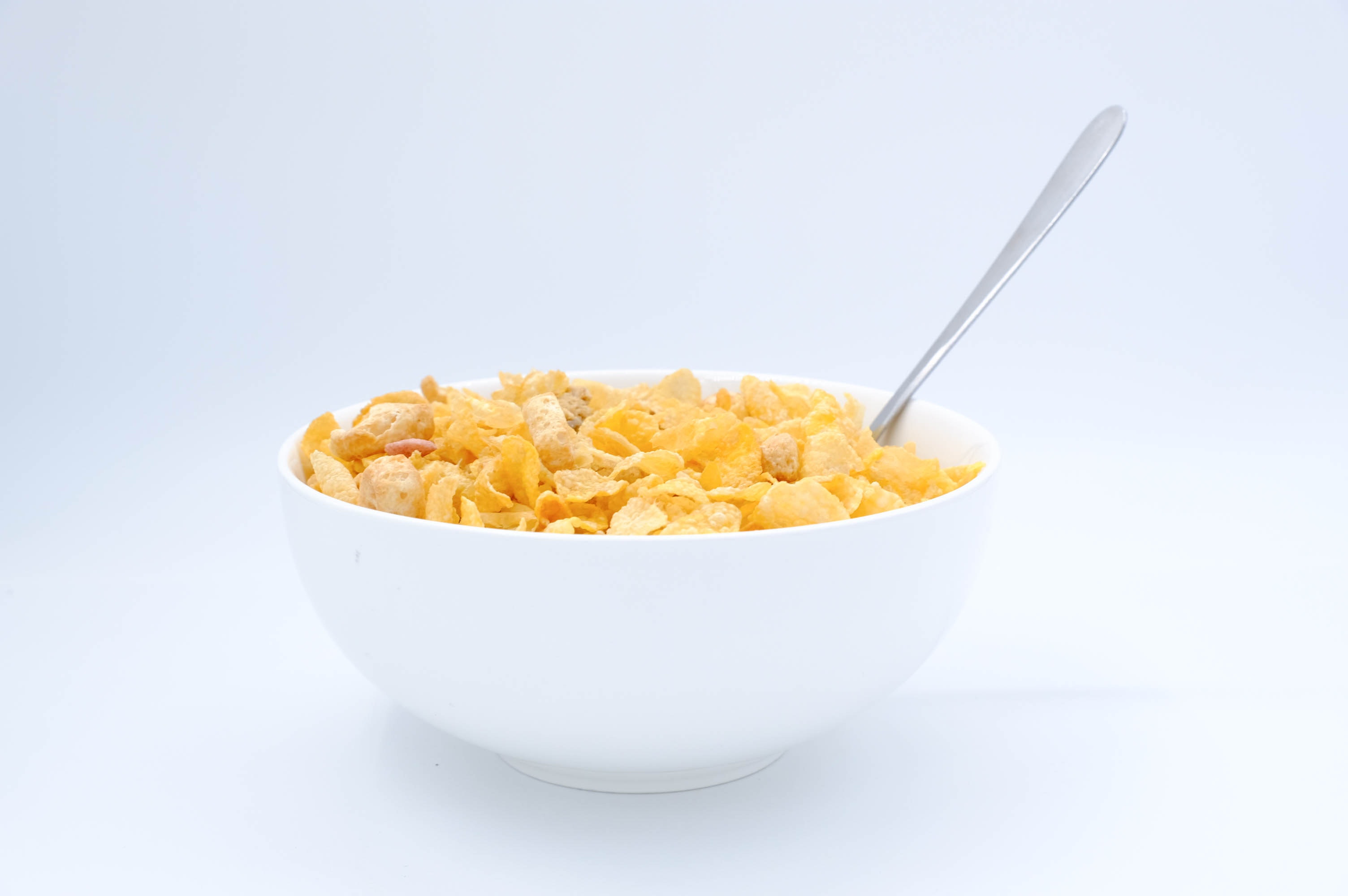 Bowl with cornflakes and spoon on white background · Free