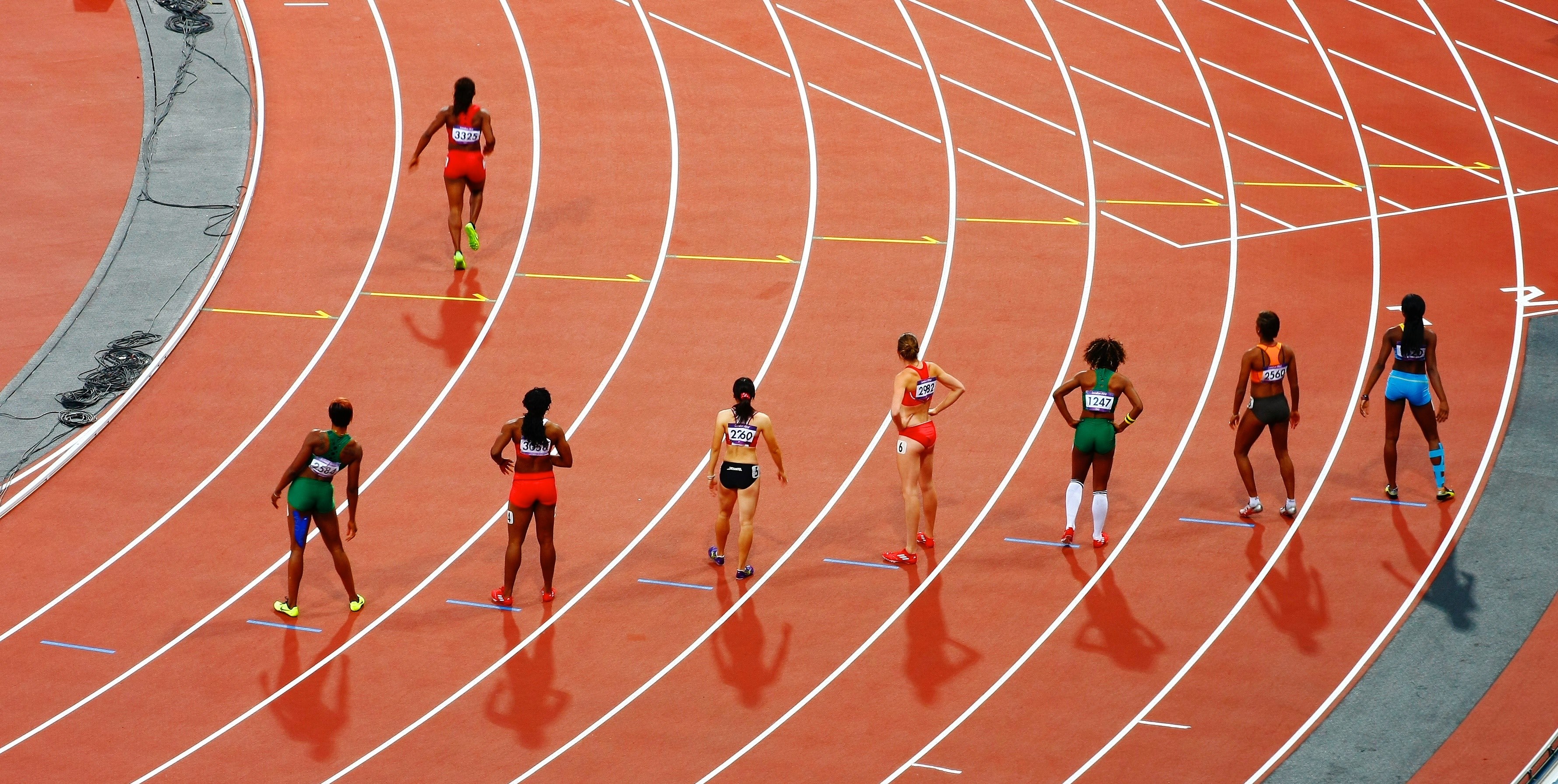Wallpaper / a woman running on a race track while seven others stand back and stretch, girls racing on track 4k wallpaper