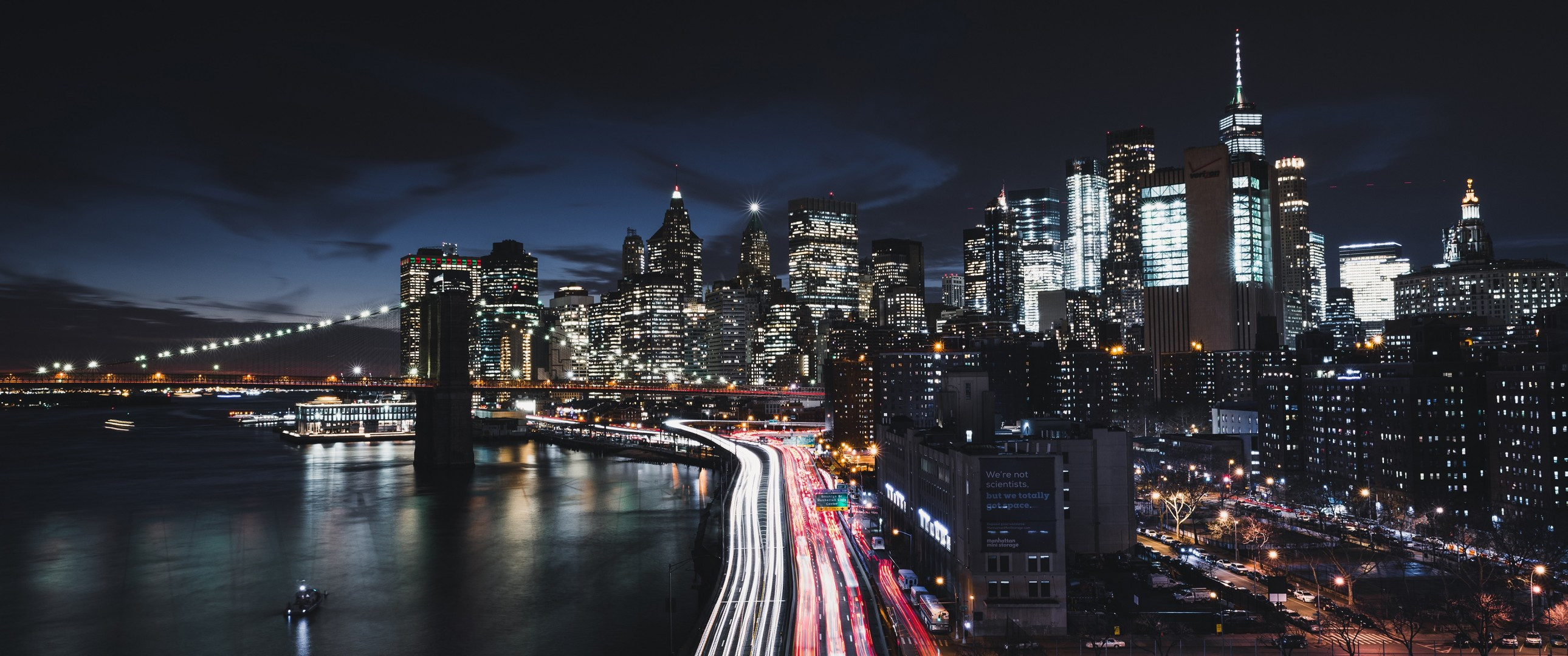 Download 2580x1080 New York City, Manhattan, Timelapse, Buildings, Night, Boat, Bridge Wallpaper