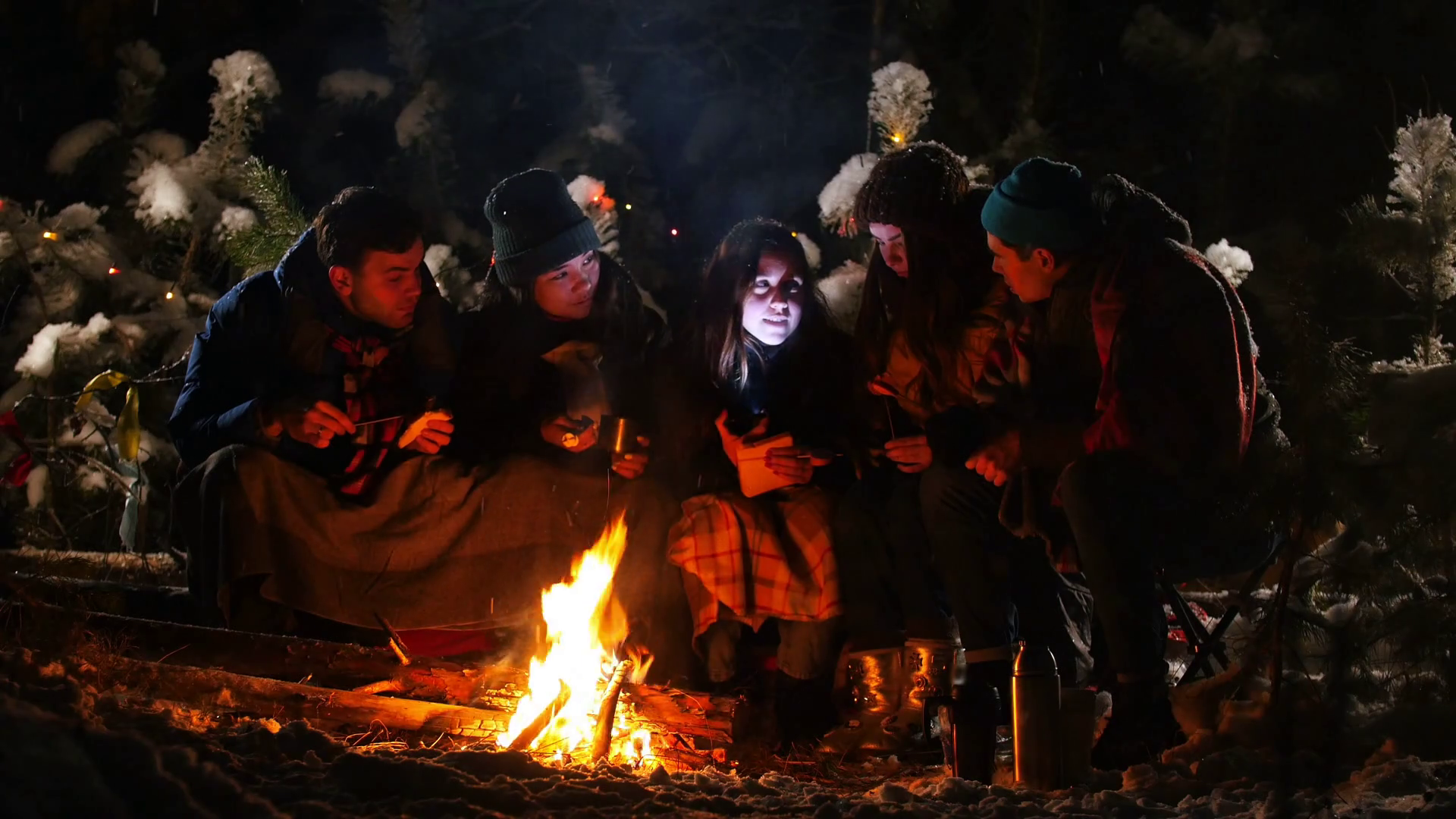 Group of friends in winter forest. Sitting near the bonfire wrapped in a blanket, listening a story and get scared Stock Video Footage