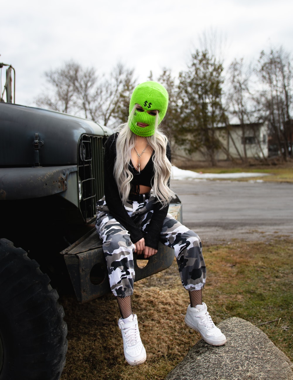 woman in green mask and black jacket sitting on gray metal tank during daytime photo