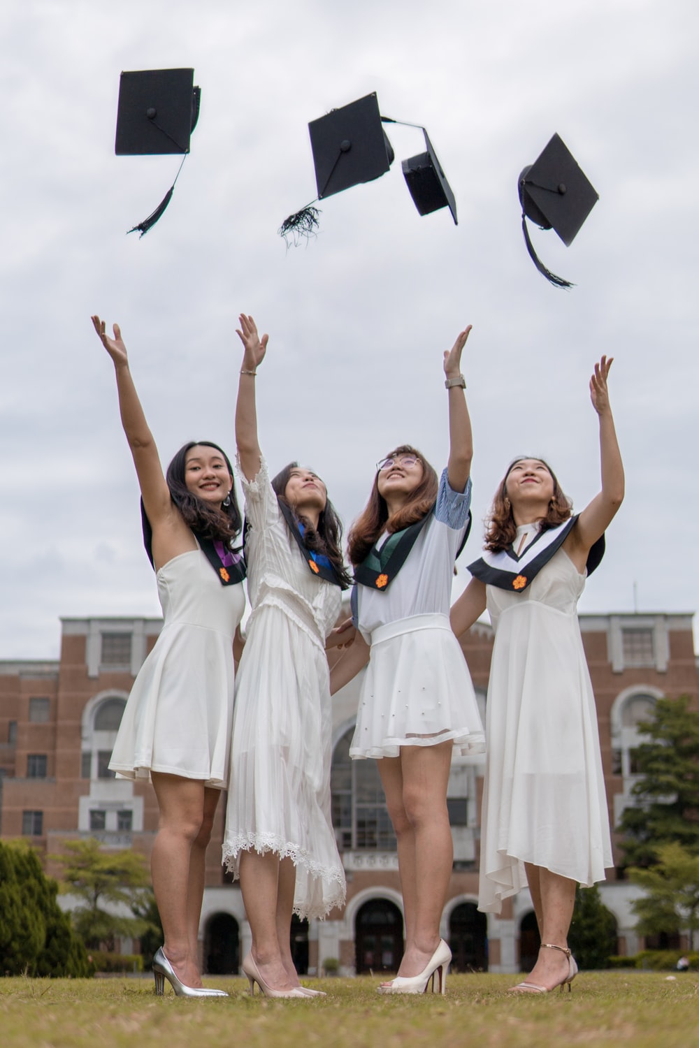 Low Angle Photography Of Four Girls Throwing Mortar Hat Near Outdoor During Daytime Photo