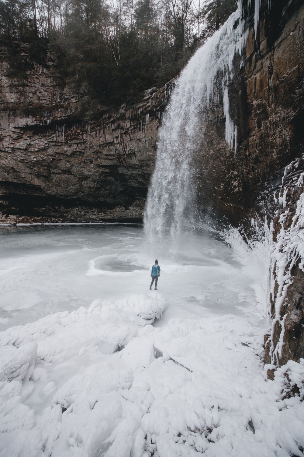 person standing on frozen waterfall outdoor during daytime photo