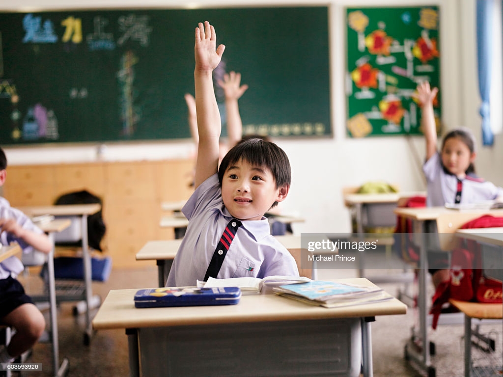 Students In Classroom Raising Hands High Res