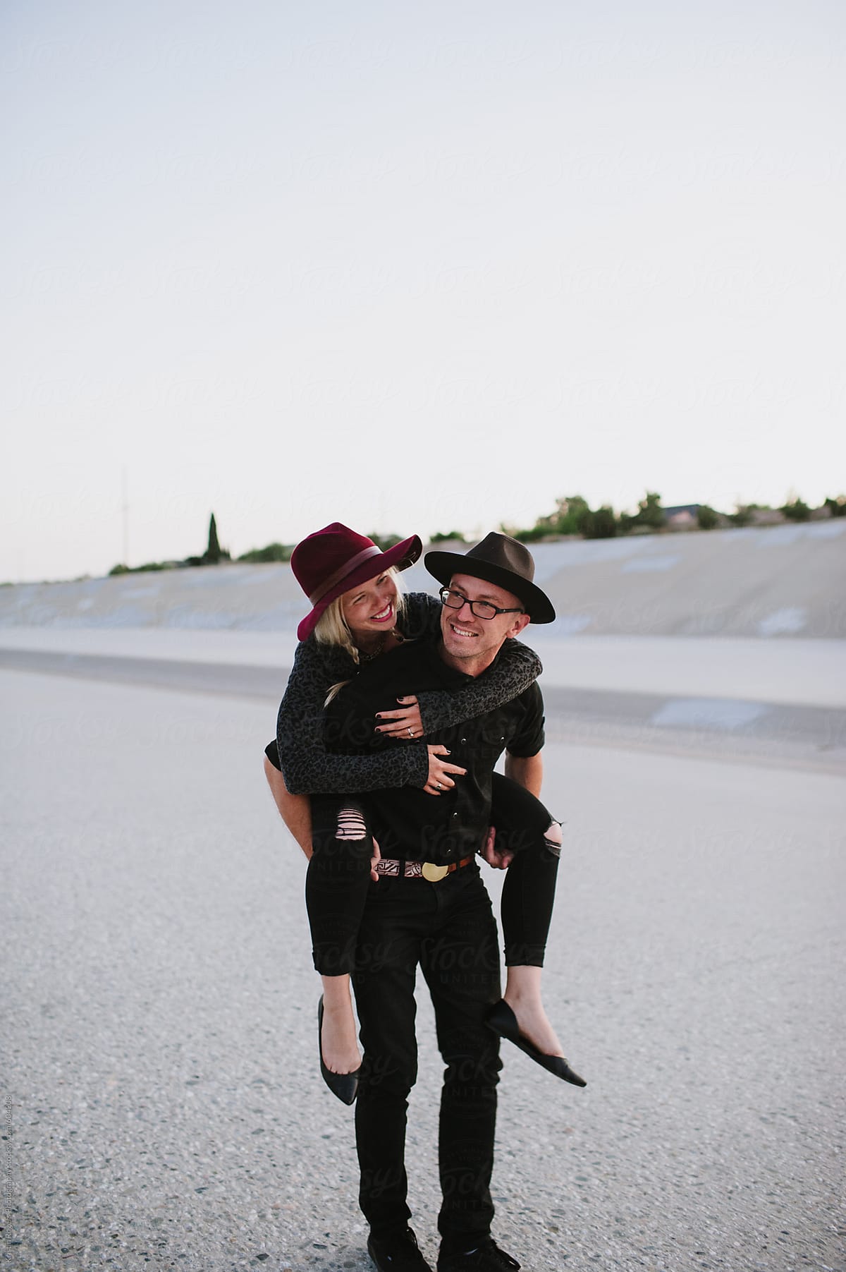 Cute Couple Wearing Hats And Giving A Piggyback Ride by Kristin Rogers Photography