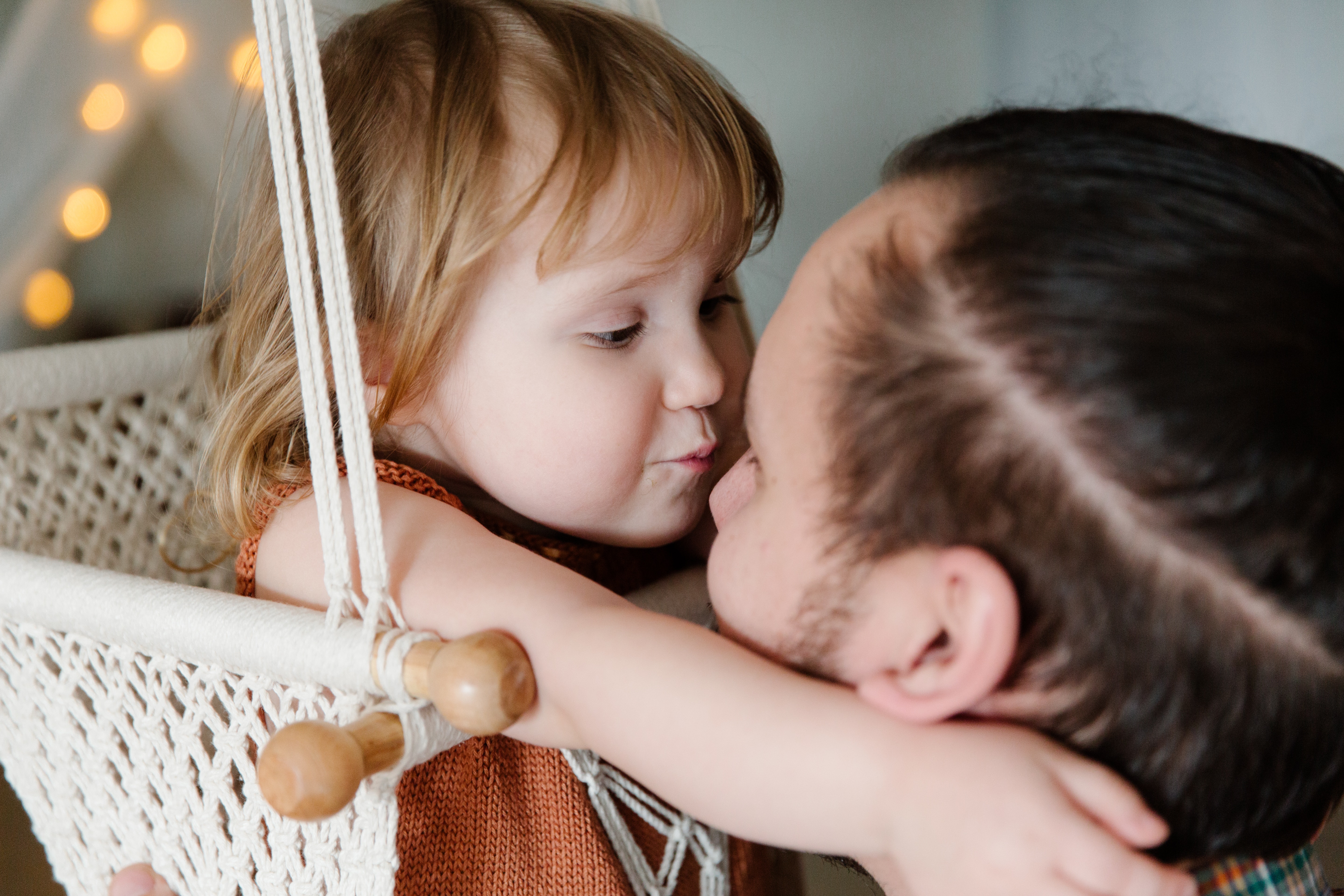 Cute kid hugging father while resting in hanging swing at home · Free