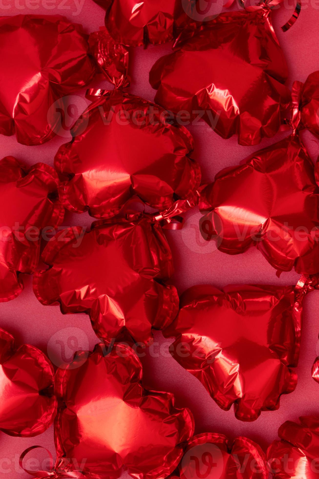 Foil balloons in the shape of a heart on pink background top view. Festive vertical background for Valentines Day