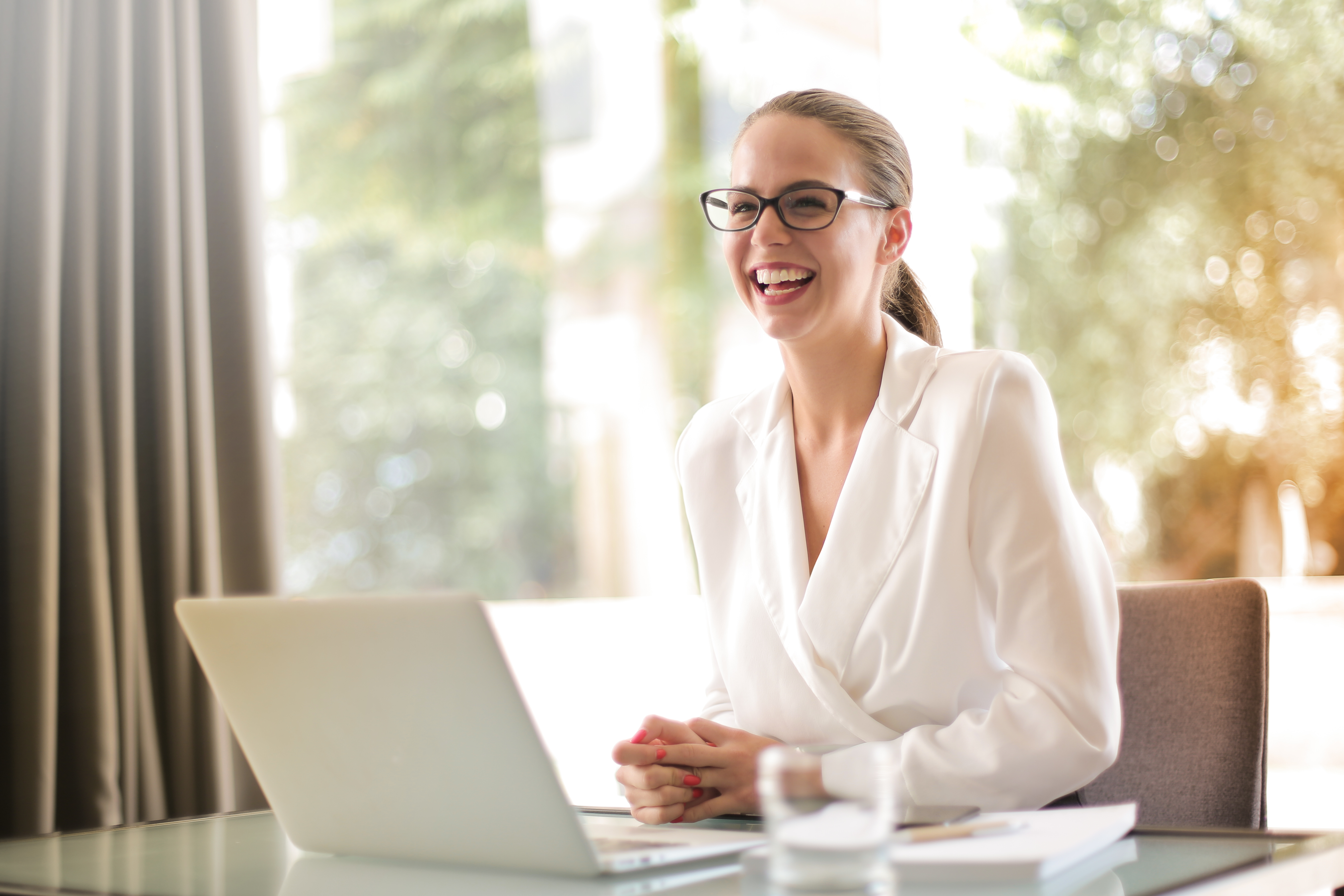 Laughing businesswoman working in office with laptop · Free