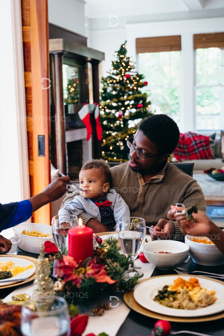 Family Eating Holiday Meal Together At Dining Room Table With Christmas Tree In Background. Diversity Photo