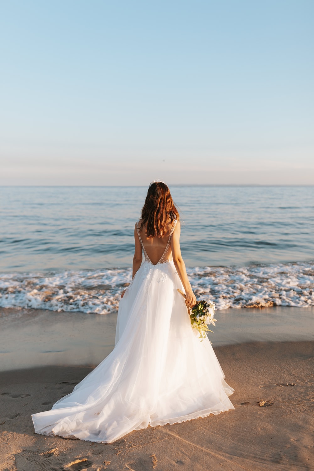 woman in white wedding dress standing on beach during daytime photo
