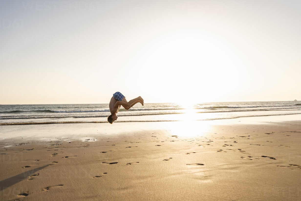 Young man doing somersaults on the beach