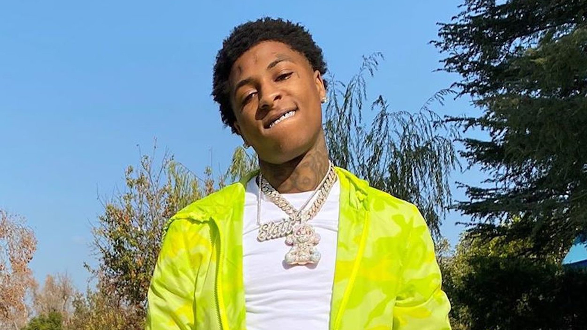 NBA Youngboy Is Wearing White T Shirt And Green Overcoat Standing In Blue Sky Background HD NBA Youngboy Wallpaper