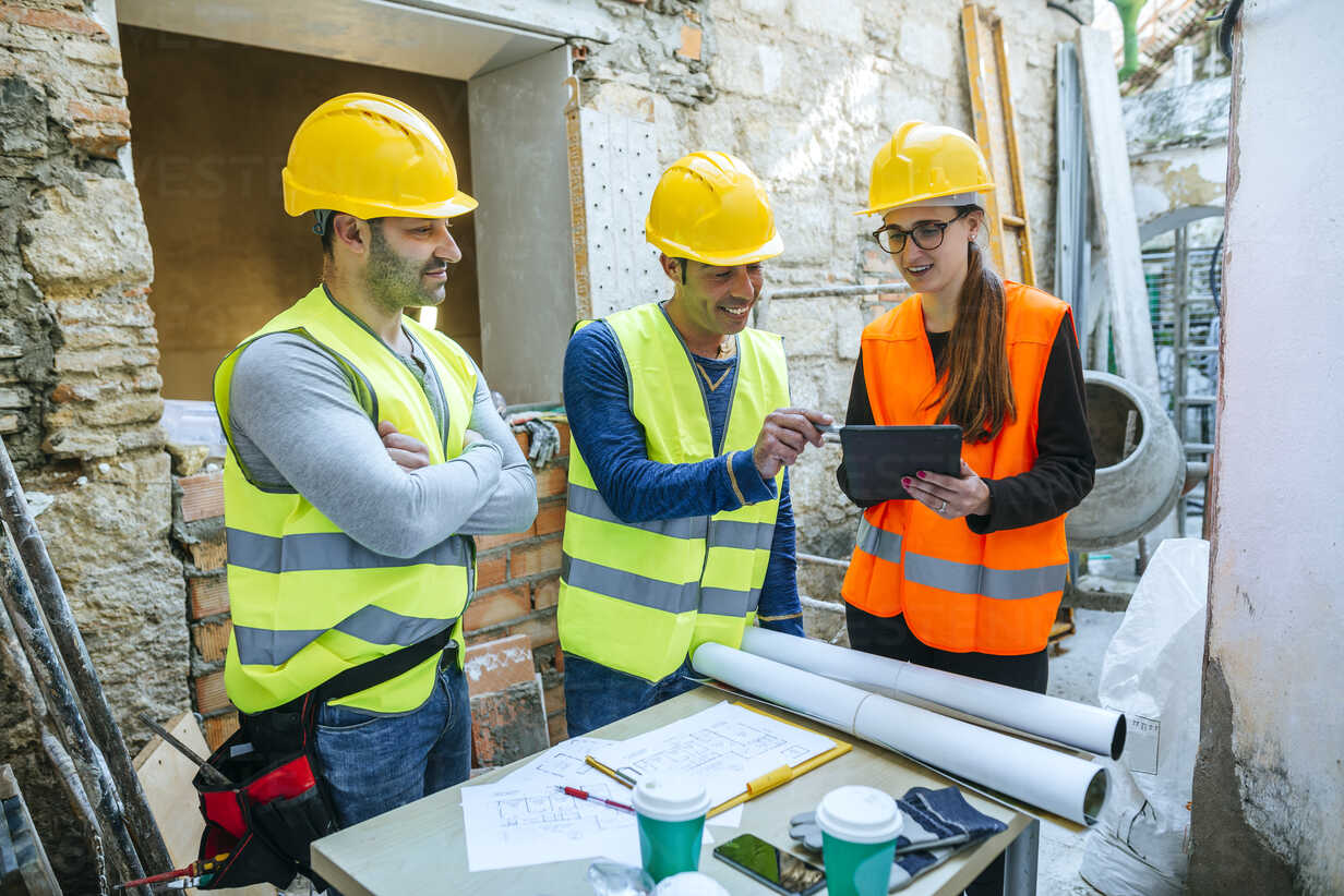 Woman and two construction workers with tablet on construction site