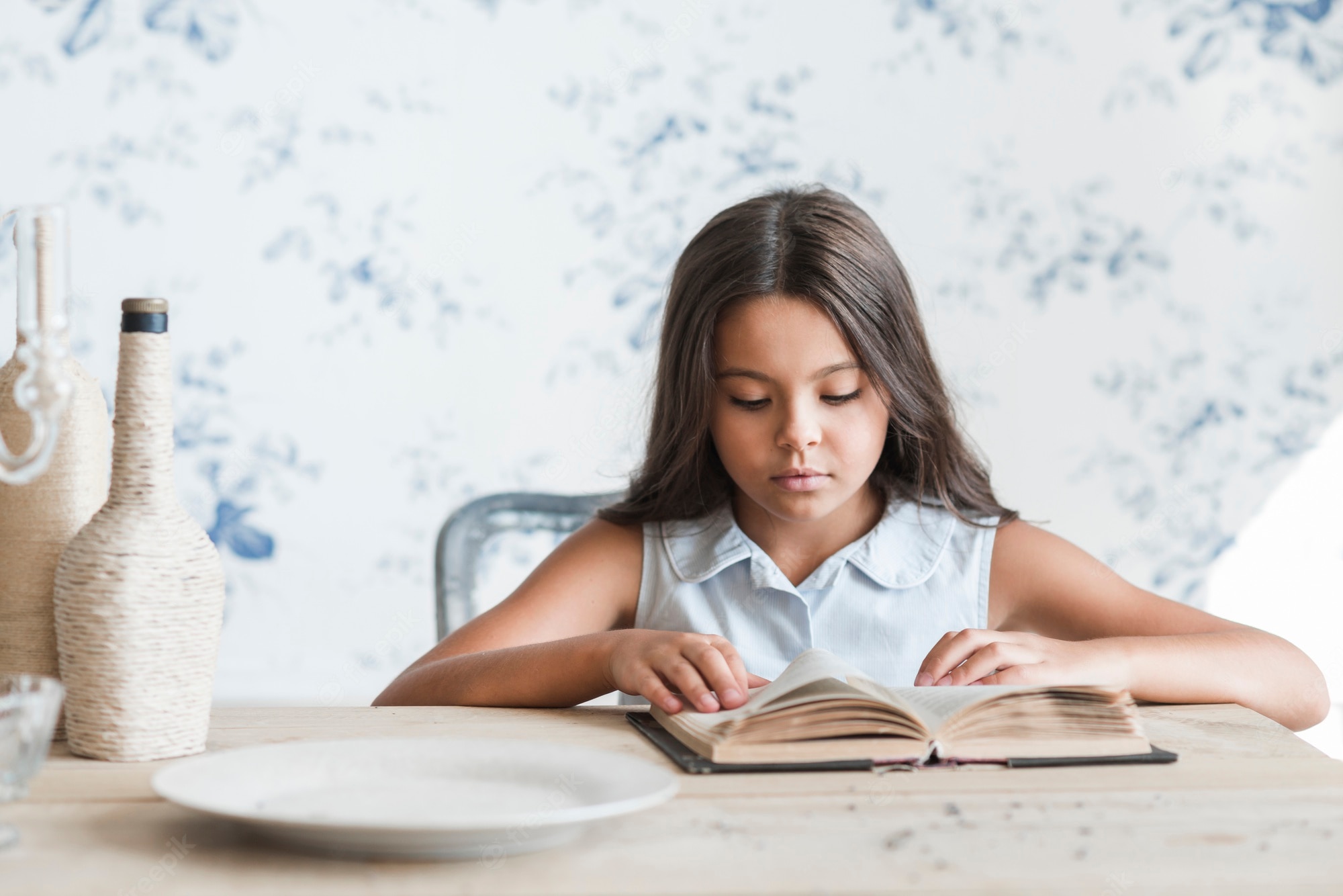 Free Photo. Portrait of a girl sitting in front of wallpaper reading book