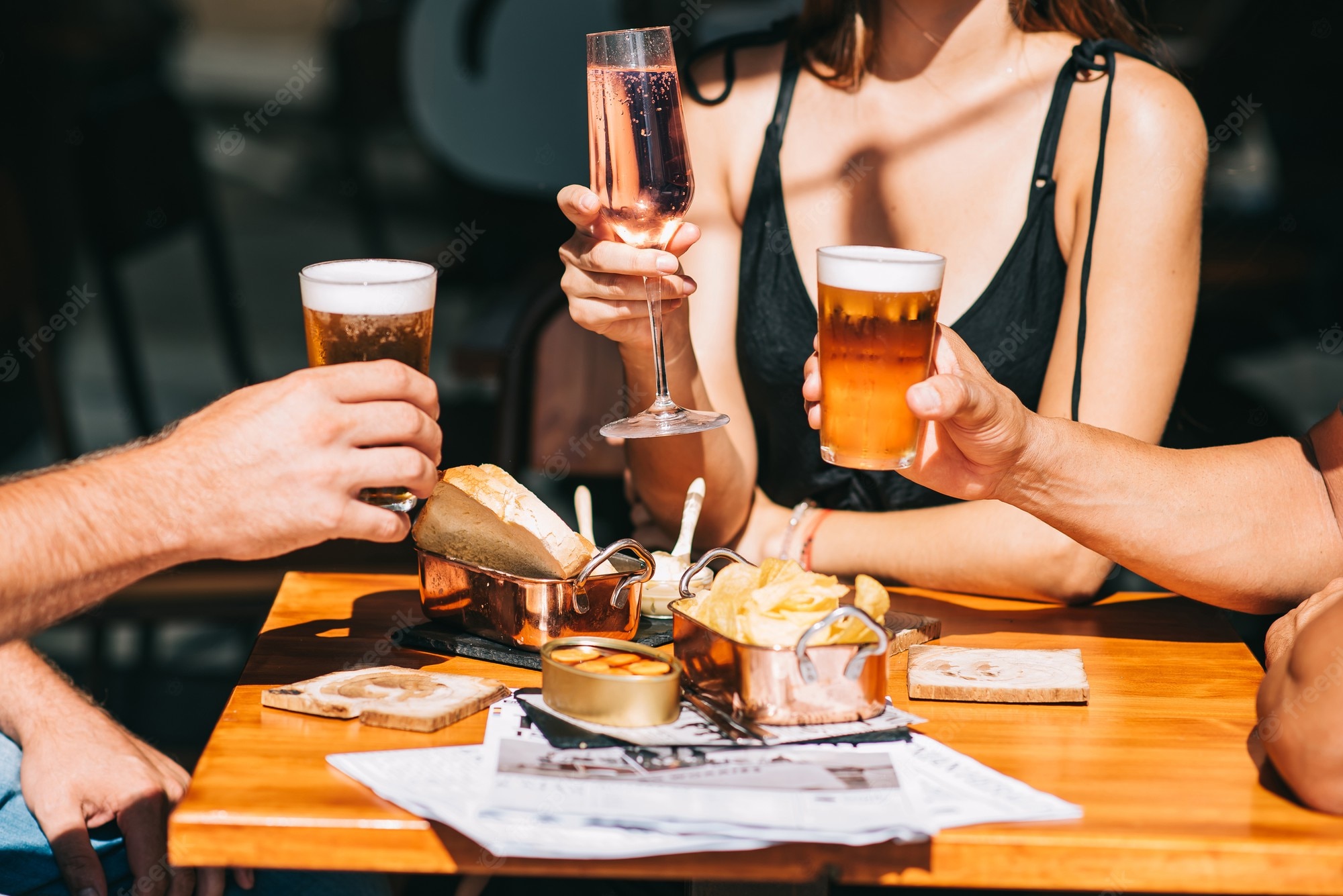 Premium Photo. Group of friends sitting on a summer terrace with beer and wine in their hands and snacks on the table