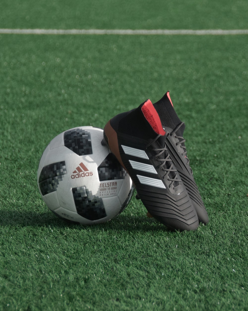 black adidas cleats lean on white and black adidas soccer ball on green grass photo