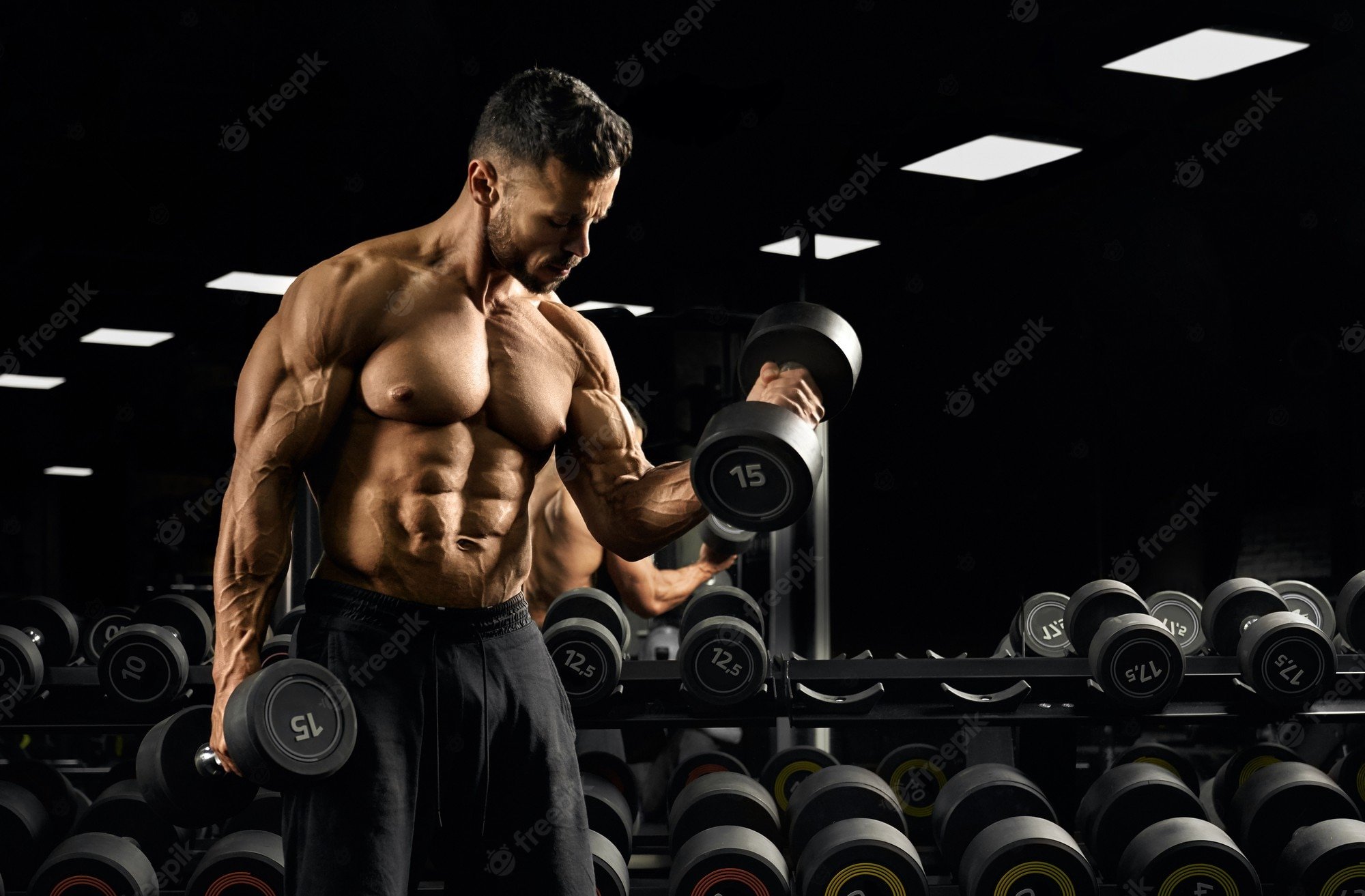 Premium Photo. Front view of shirtless bodybuilder training biceps with weights near stand with dumbbells