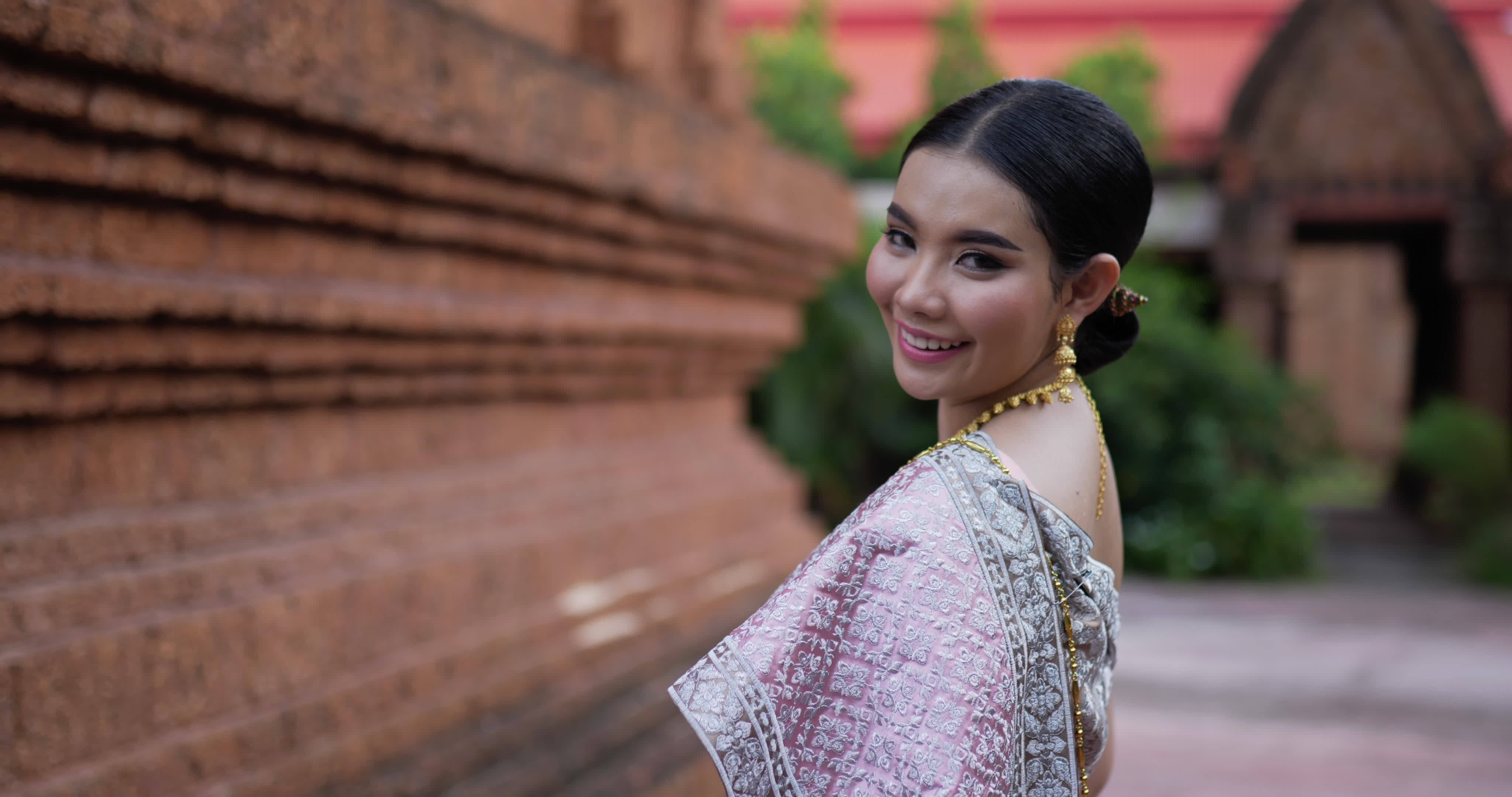 Portrait of Thai woman in traditional costume looking at camera and walking in ancient temple