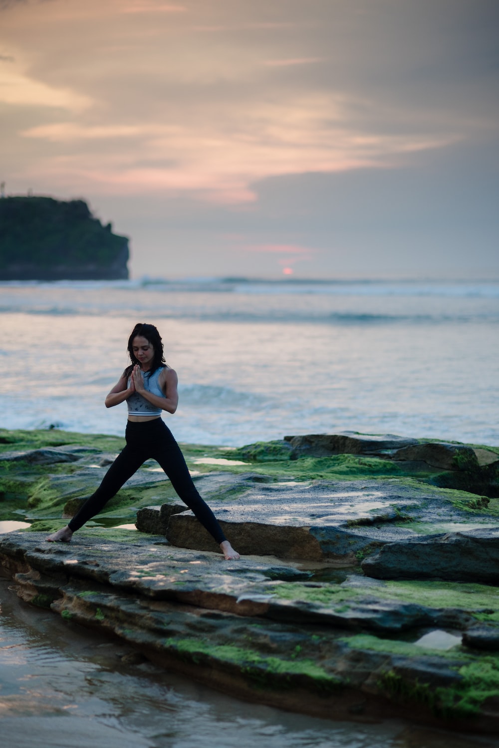 woman doing yoga on rock platform next to body of water photo