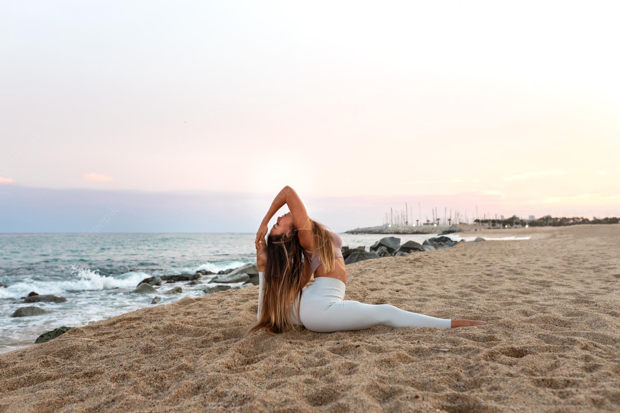 Premium Photo. Flexible young caucasian woman practicing the splits yoga pose on the beach at sunset copy space