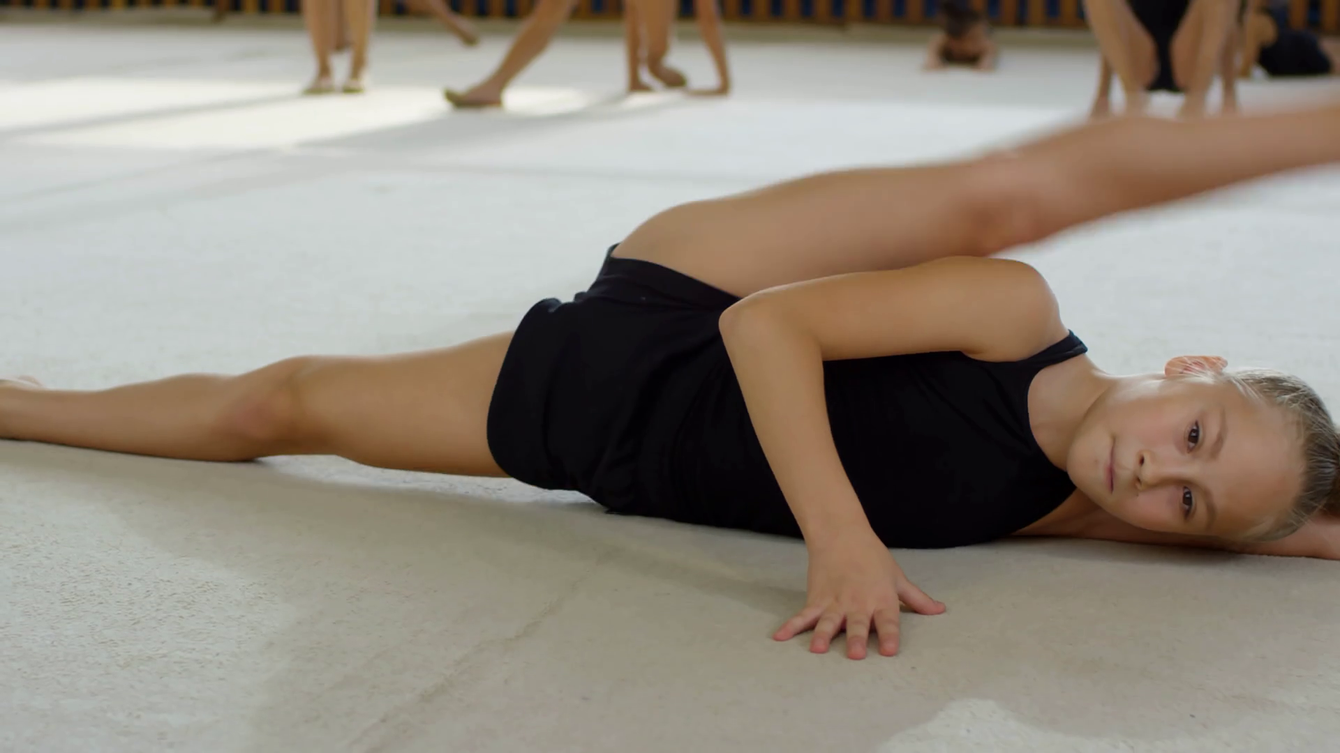 Portrait Of Flexible Young Girl Of Elementary School Age Lying On Floor, Stretching Leg Muscles And Looking At Camera Stock Video Footage 00:23 SBV 337878268
