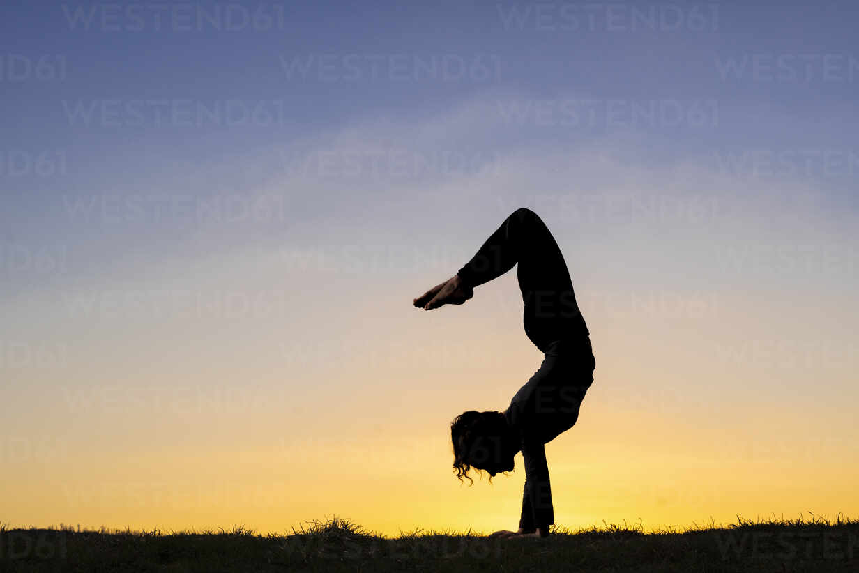 Flexible young woman in silhouette doing handstand