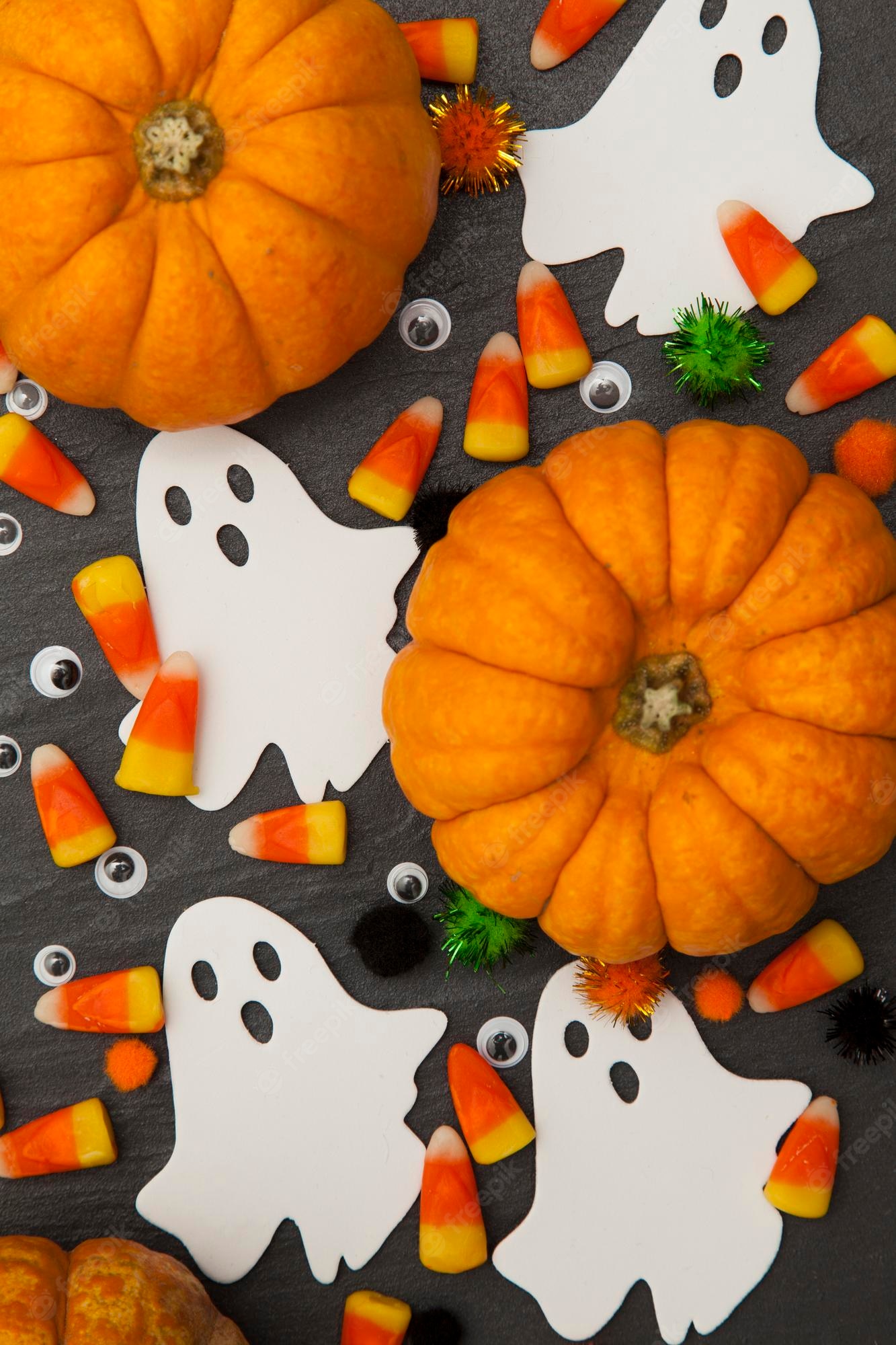 Premium Photo. Halloween background with ghosts and candy corn on a slate background