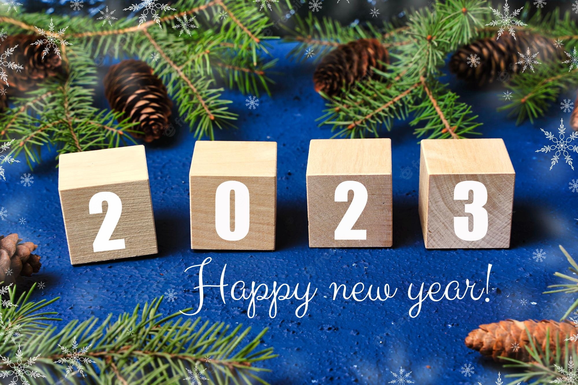 Premium Photo. Happy new year 2023 text sign on wooden cubes with frame of christmas tree branch and cones on red background snowflakes