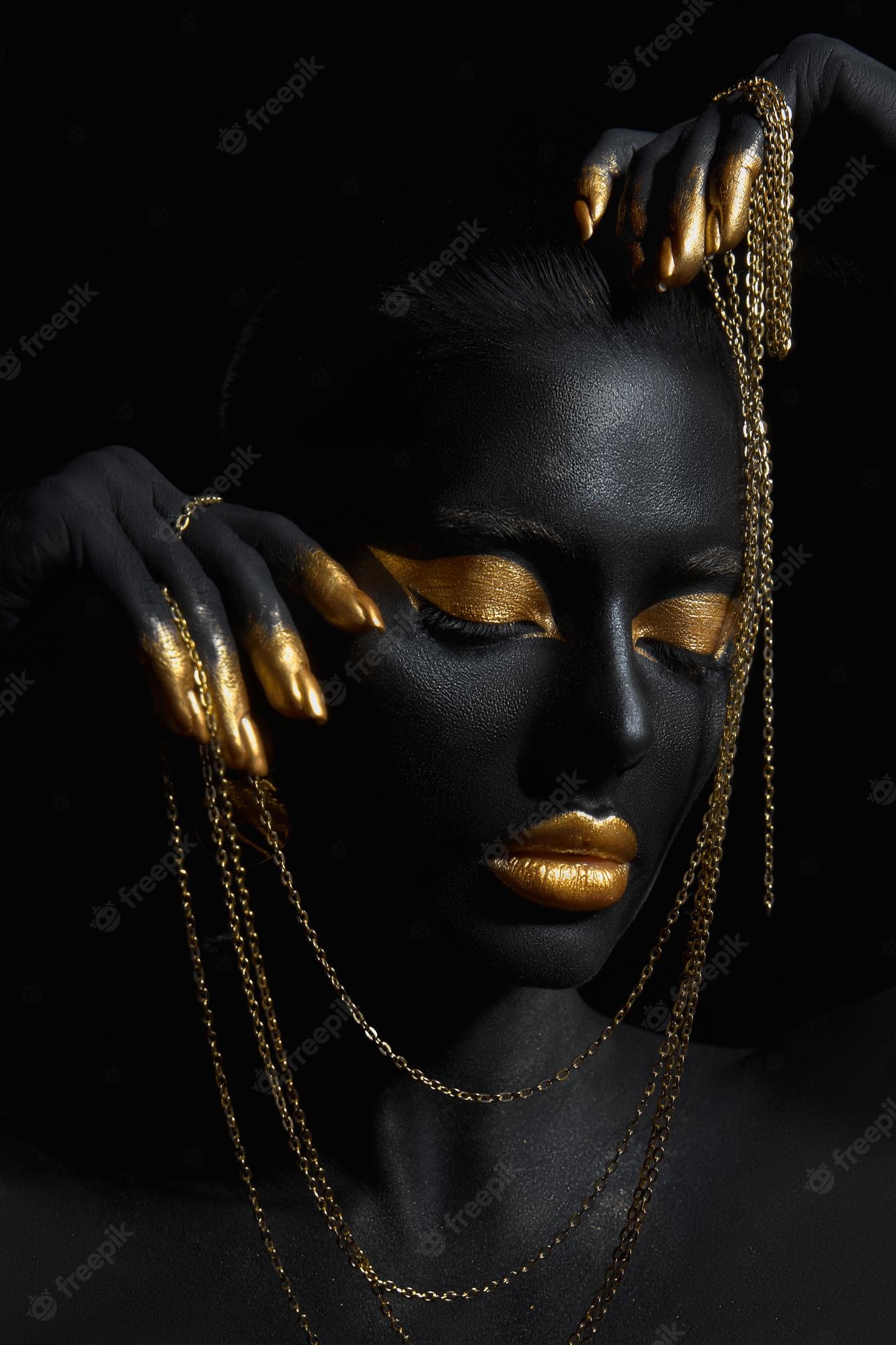 Premium Photo. Beauty woman painted in black skin color body art, gold chain in his hands and around his neck. gold makeup lips eyelids, fingertips nails in gold color paint. professional