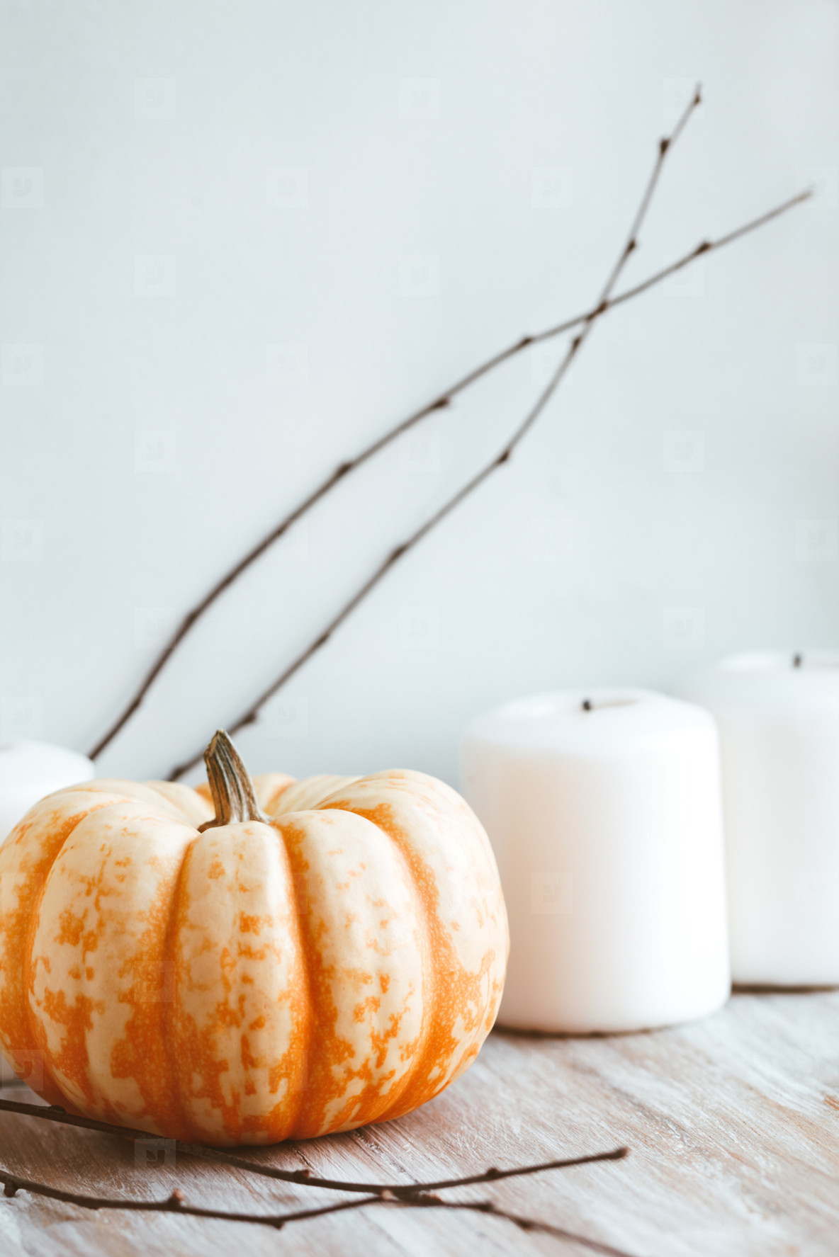 Small pumpkin and white candles still life near white wall. Autumn background
