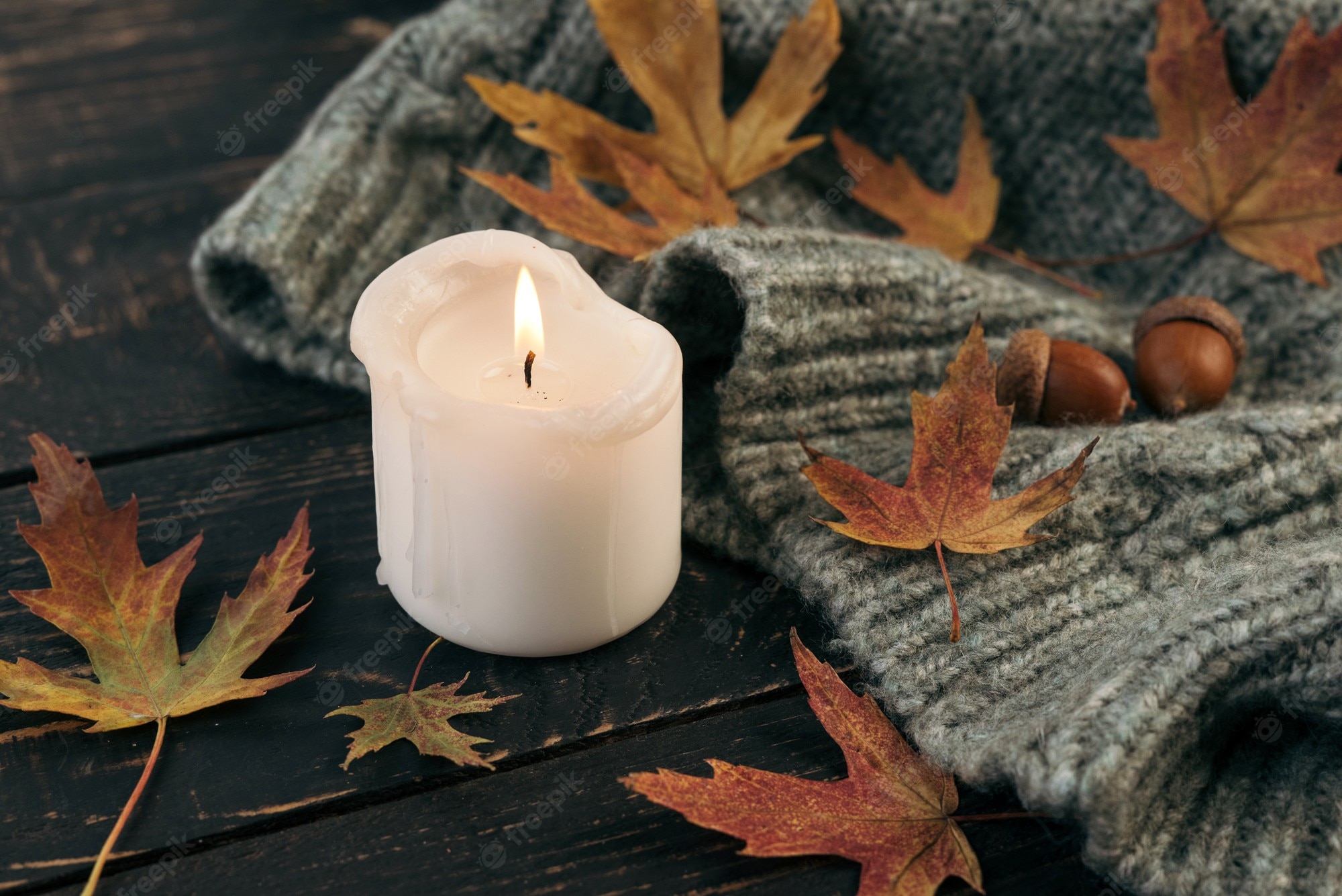 Premium Photo. Cozy and autumnal atmosphere. a candle is burning against the background of a knitted blanket with fallen autumn leaves on a dark wooden table