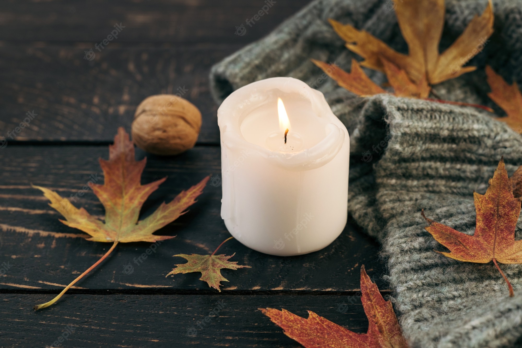 Premium Photo. Cozy and autumnal atmosphere. a candle is burning against the background of a knitted blanket with fallen autumn leaves on a dark wooden table