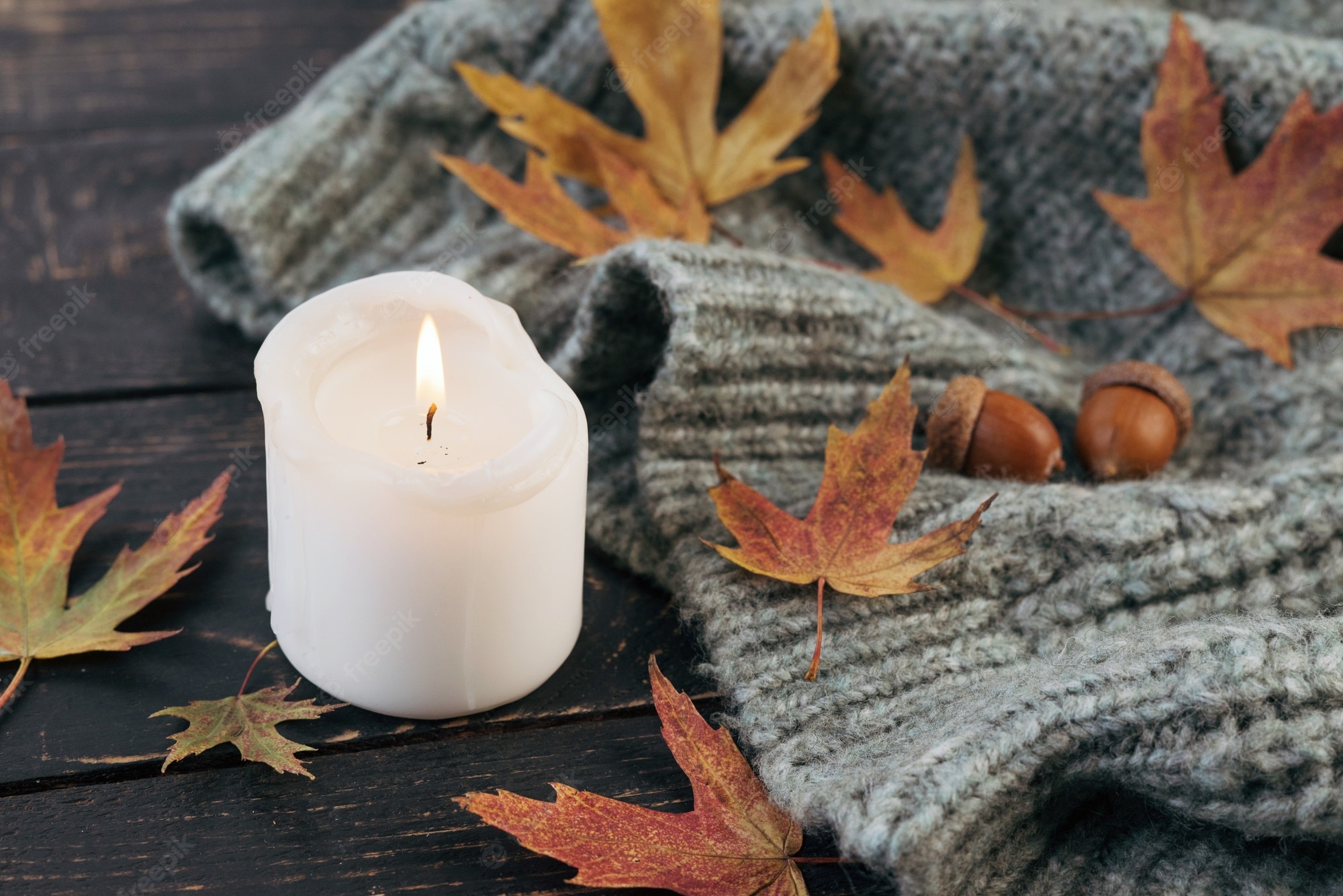 Premium Photo. Cozy and autumnal atmosphere. a candle is burning against the background of a knitted blanket with fallen autumn leaves on a dark wooden table