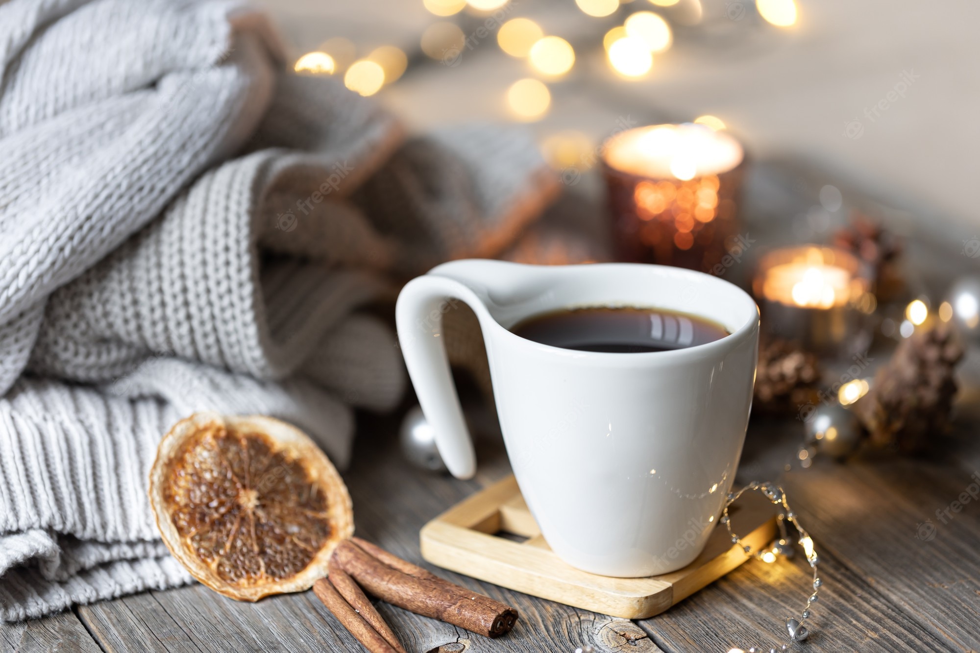 Free Photo. Cozy home winter composition with a cup of tea on a blurred background with burning candles and bokeh lights and knitted elements
