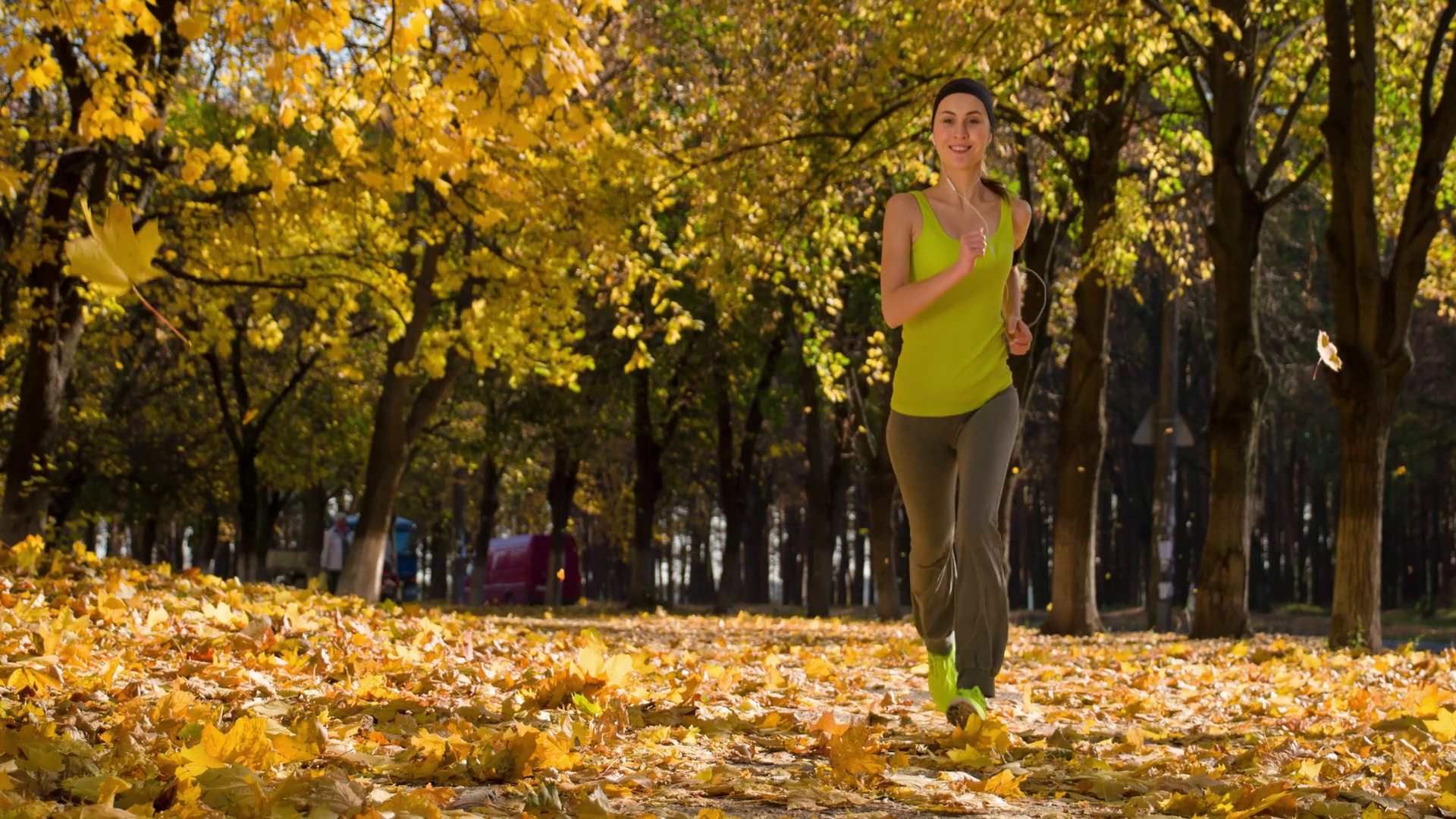 Running woman. Runner is jogging in sunny bright light in the autumn park background. Female fitness model training outside on a warm fall day and listening to music. Sport lifestyle. 4k slow