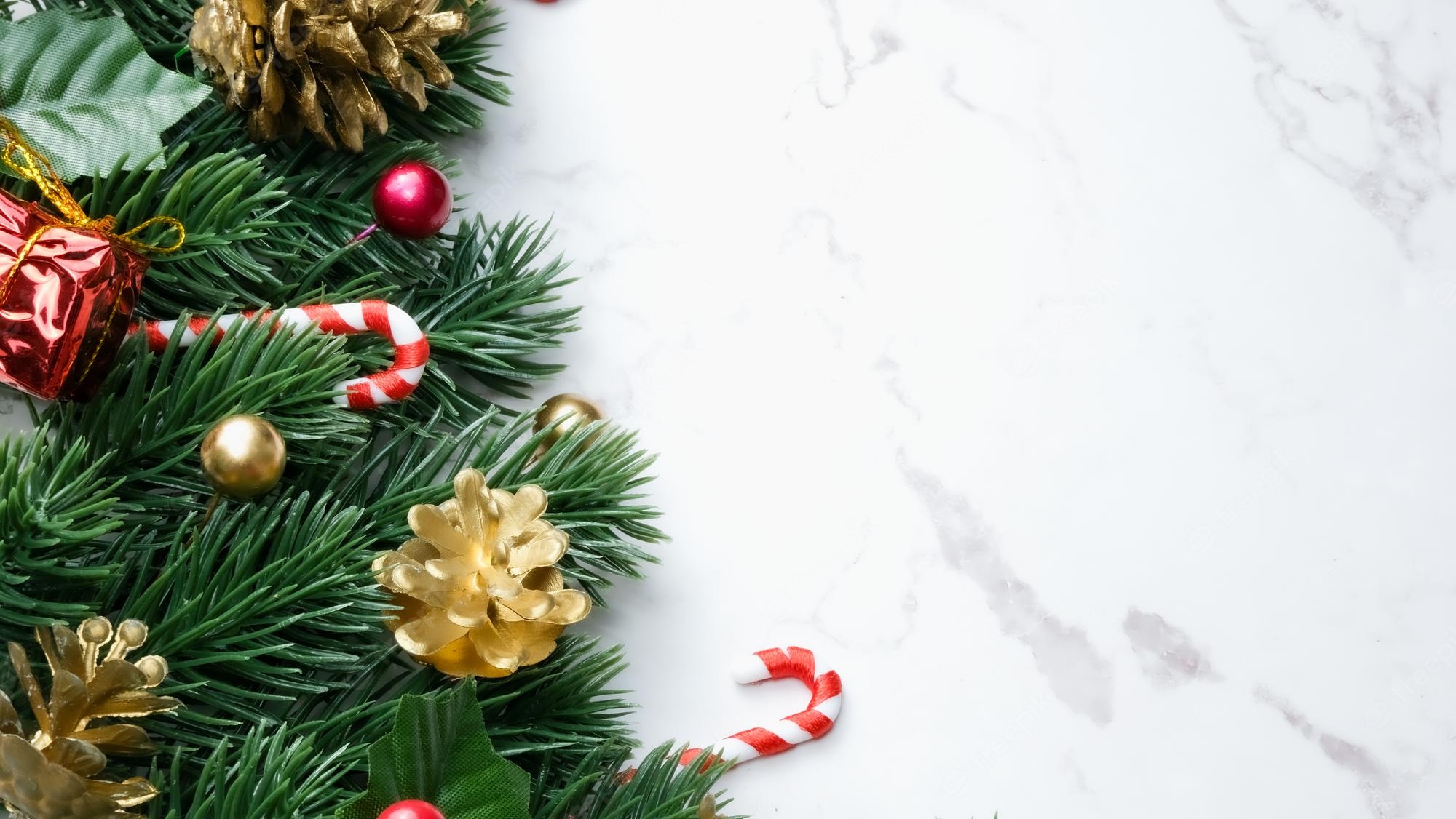 Premium Photo. Green pine tree leaves, red christmas decorations and candy canes on white marble background, christmas decorations in bright red color. simple and creative christmas concept