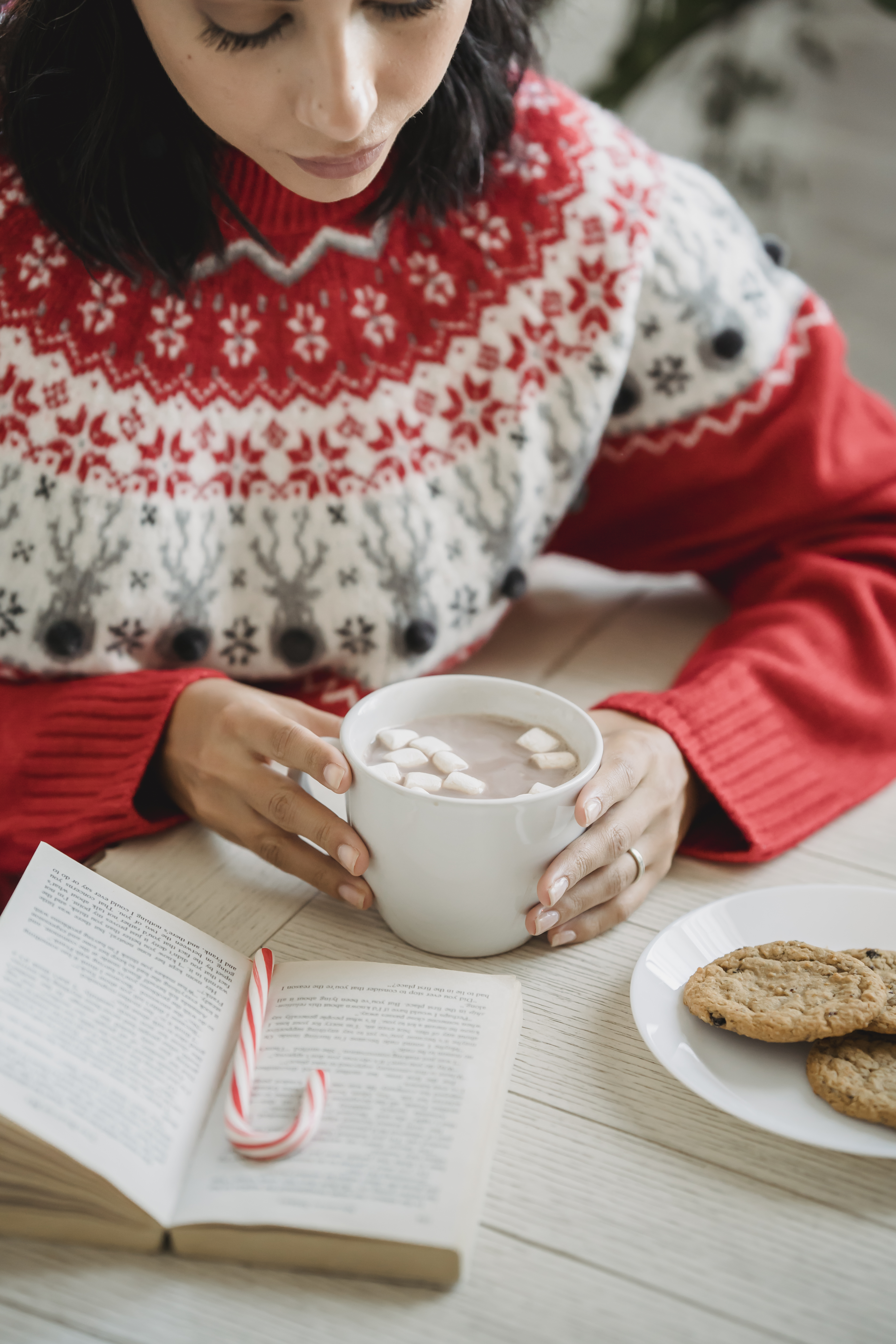 Crop woman enjoying hot chocolate and reading book at table during Christmas · Free