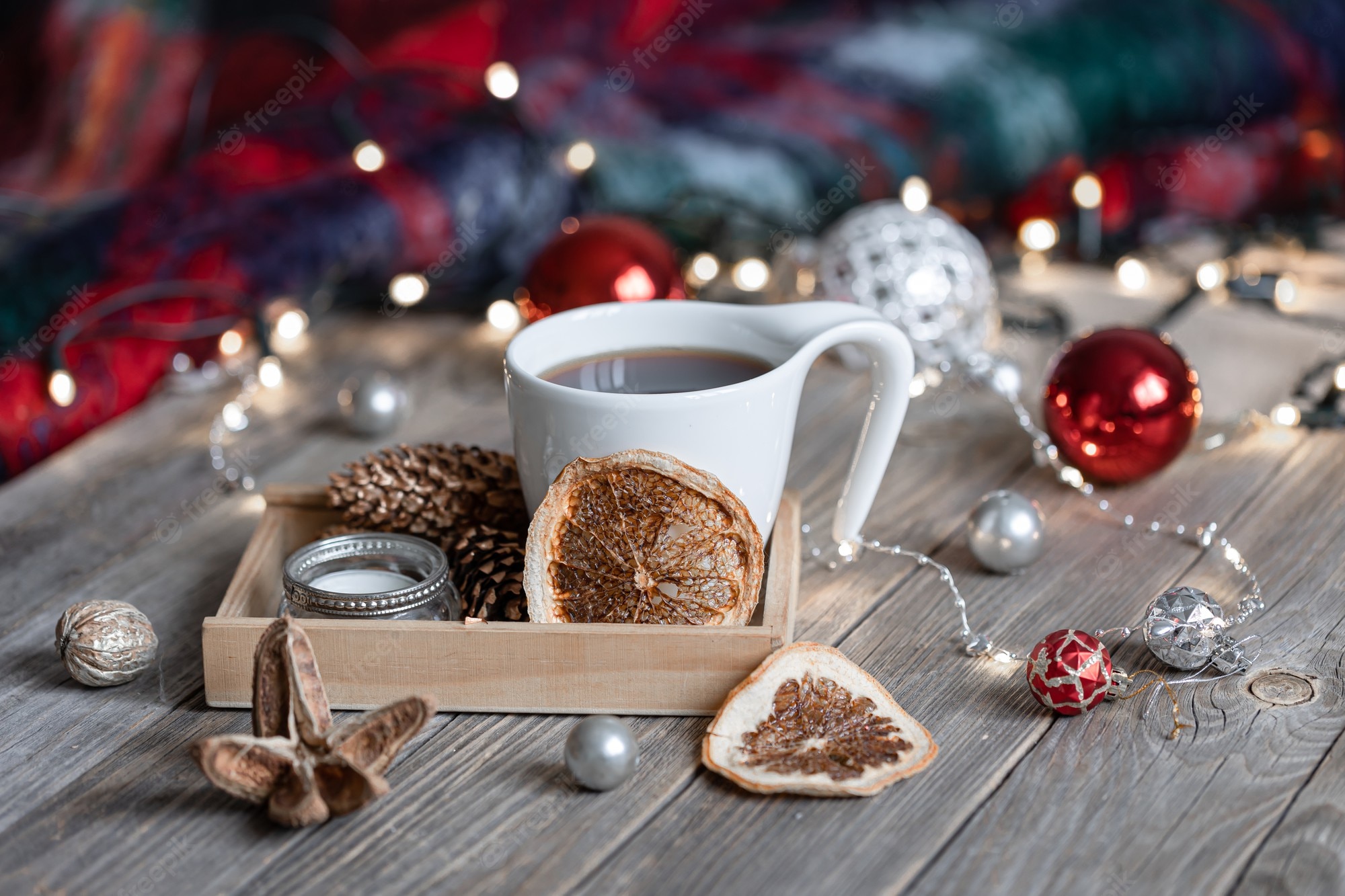 Free Photo. Cozy winter composition with a cup of hot drink, decorative details and christmas balls on a blurred background with bokeh