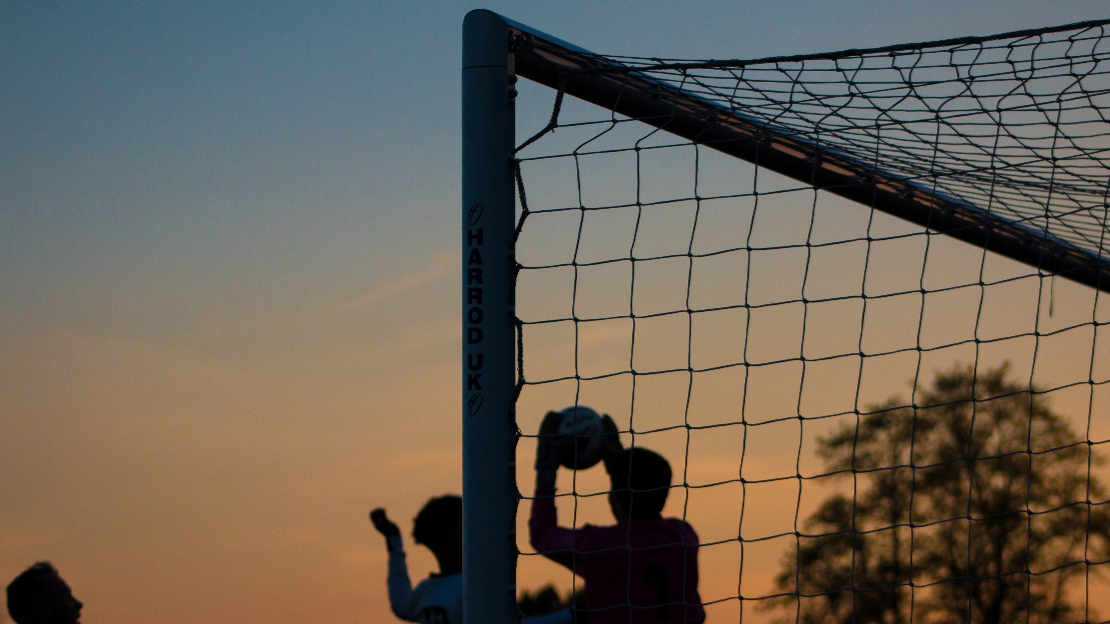 Wallpaper / three children play soccer at sunset at ewen fields, silhouette goalkeeper catching the ball 4k wallpaper free download